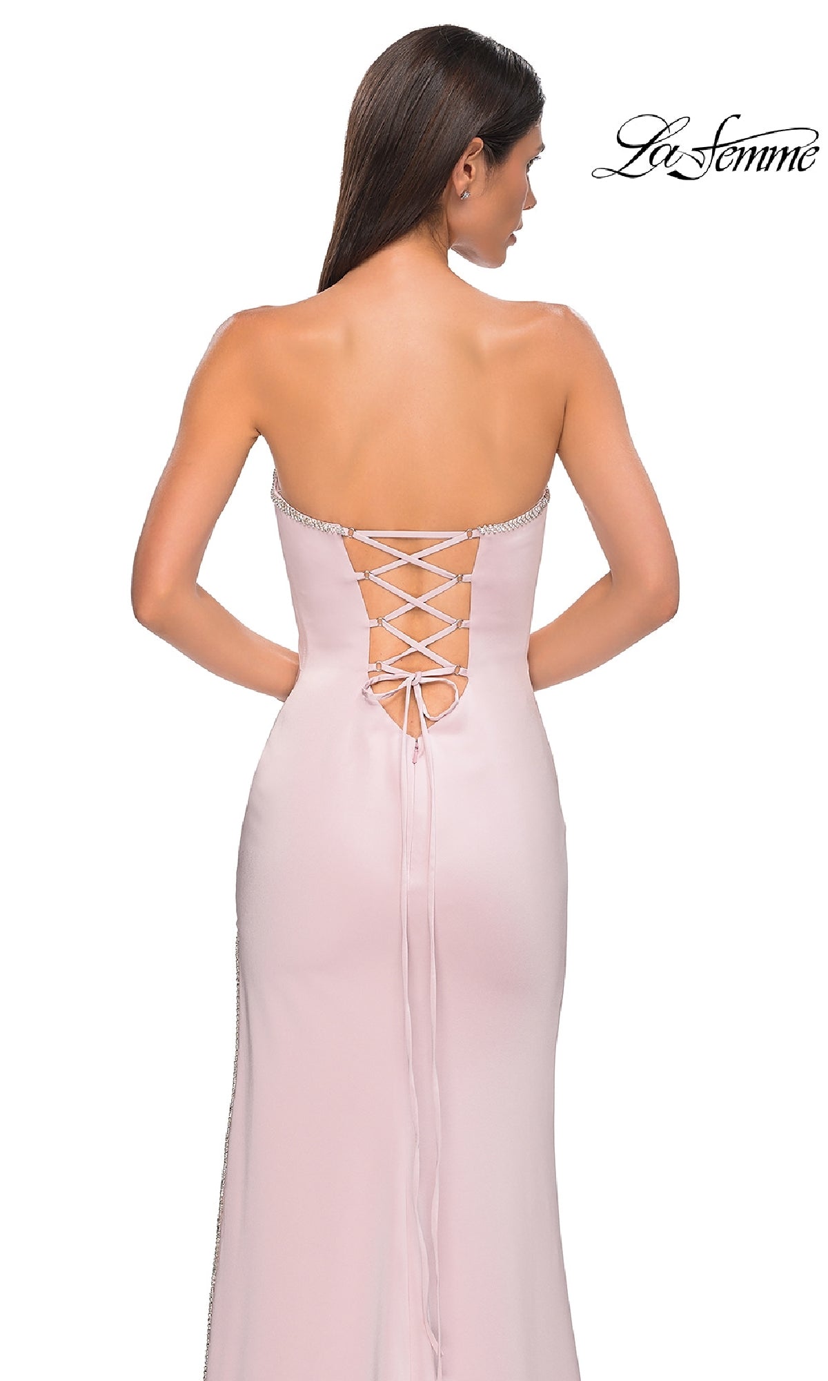 A woman stands with her back to the camera wearing the Classic Strapless Long Prom Dress: La Femme 32799 in pale pink, featuring a lace-up back detail.