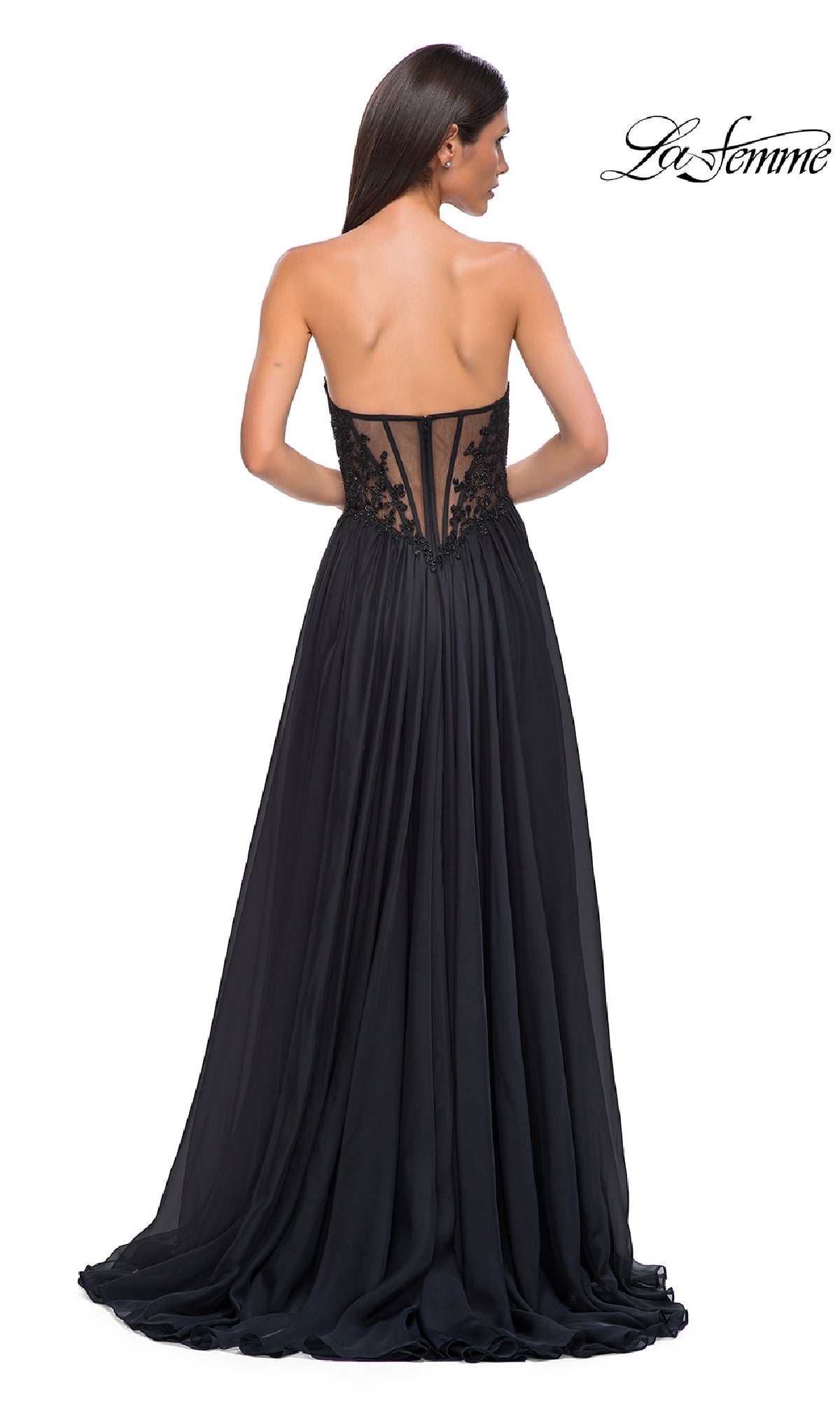 A woman models the La Femme 32804 Strapless Long A-Line Prom Dress, a floor-length black gown with a sheer back panel and lace detailing, standing with her back to the camera.