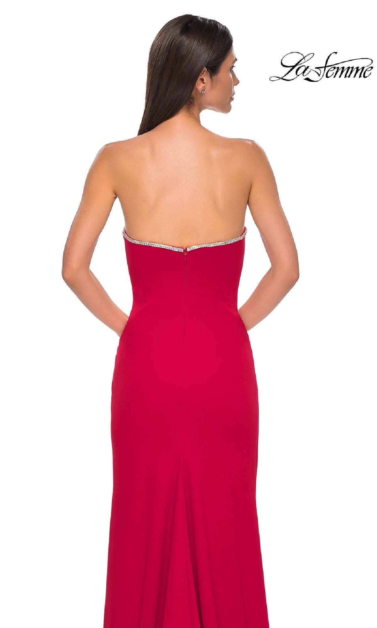 A woman stands with her back to the camera, radiating elegance in the Strapless Long Jersey Prom Dress La Femme 32854, which features jeweled trim, against a white background.