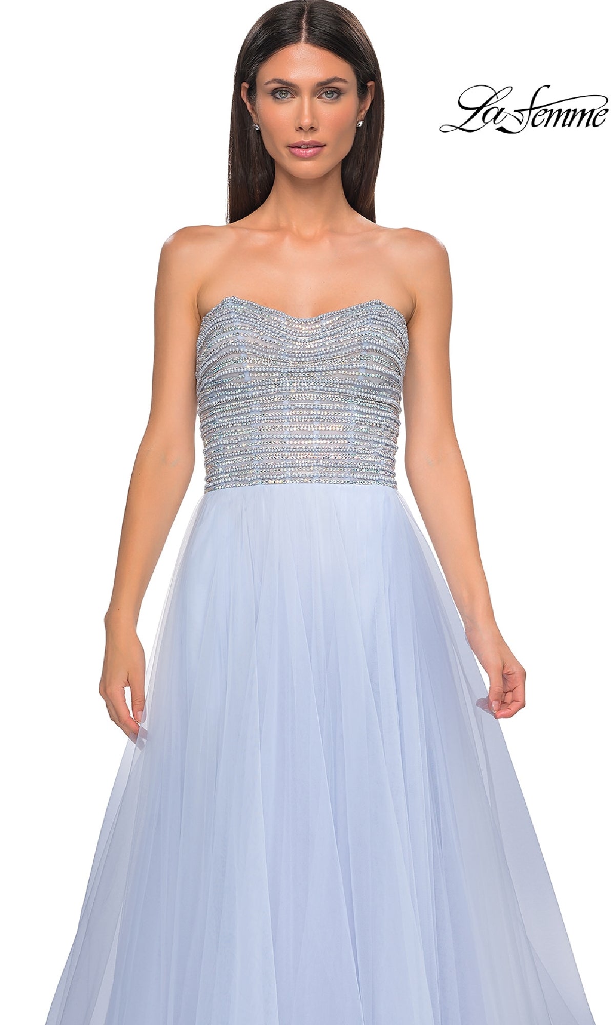 A woman wears the Strapless Long Prom Ball Gown: La Femme 32875 in light blue, featuring a beaded bodice and flowing tulle skirt, standing against a plain white background. The