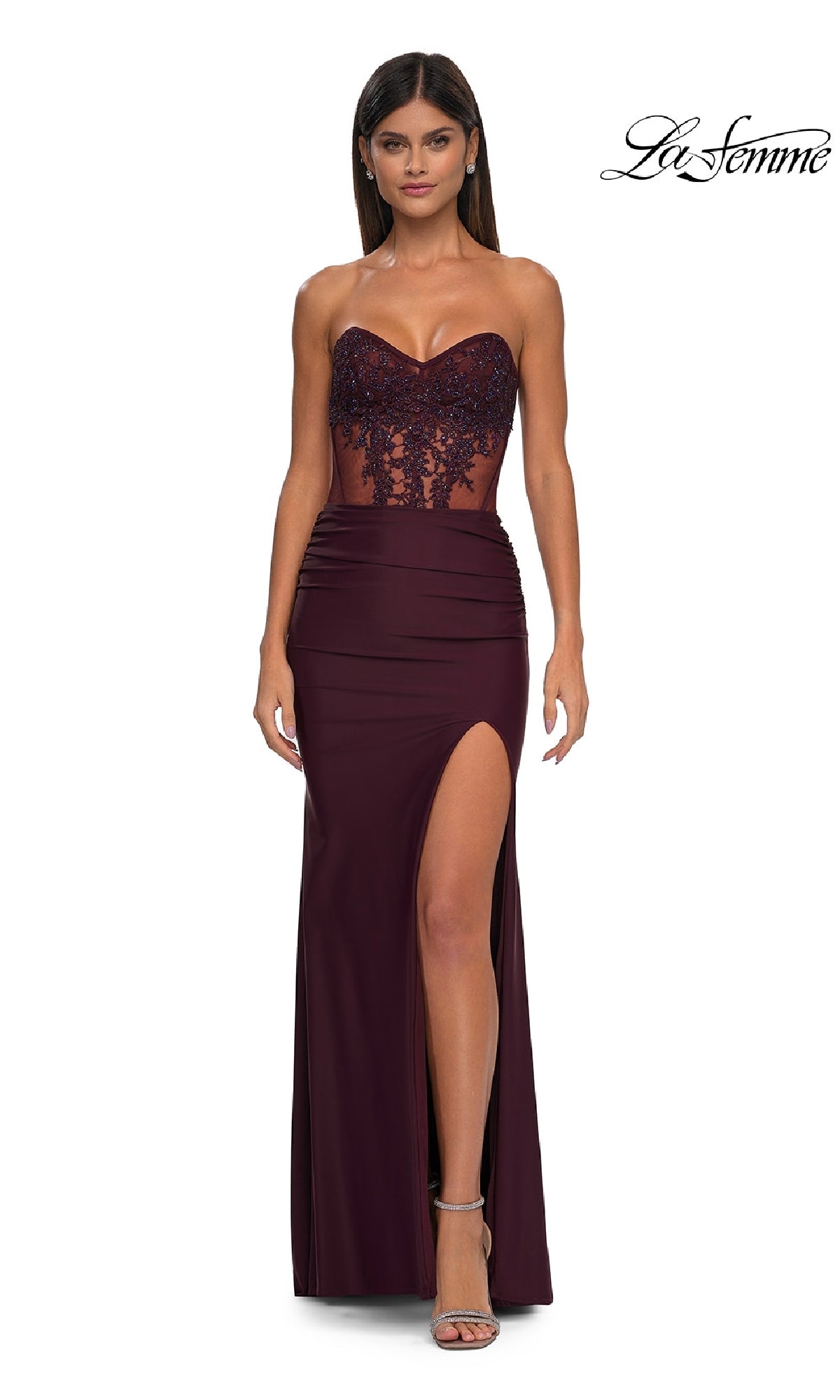 A woman wears the Dark Wine Sheer-Waist Long Corset Prom Dress (La Femme 32912) with a beaded lace bodice and high slit, standing against a white background with the