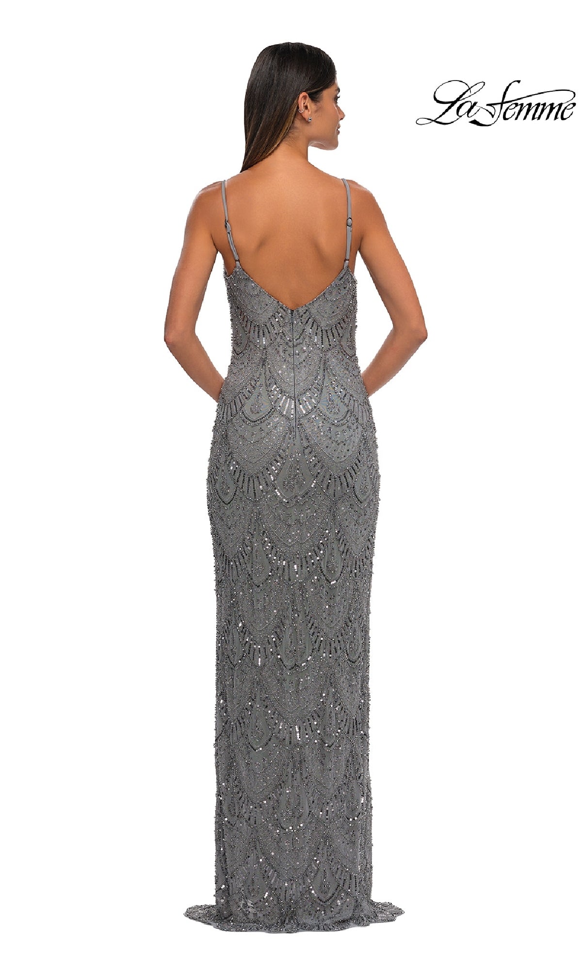 A woman stands facing away in the Vintage Long Beaded Prom Dress: La Femme 32928, a floor-length silver sequin gown with thin straps and an intricate pattern, radiating timeless elegance.