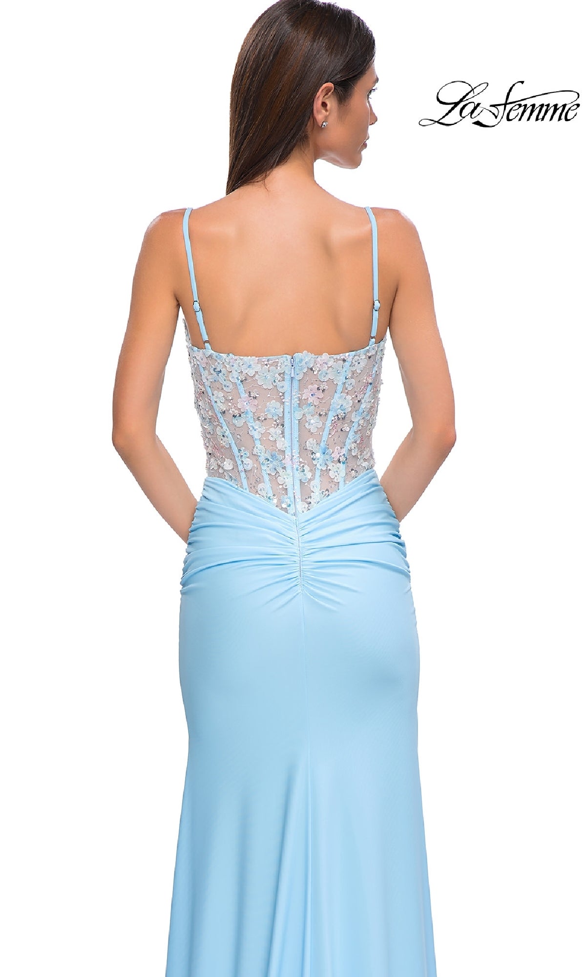A woman is shown from the back wearing the Light Blue Prom Dress: La Femme 32957, featuring thin straps, a sheer corset bodice, ruched detailing, a fitted silhouette, and delicate floral lace accents.