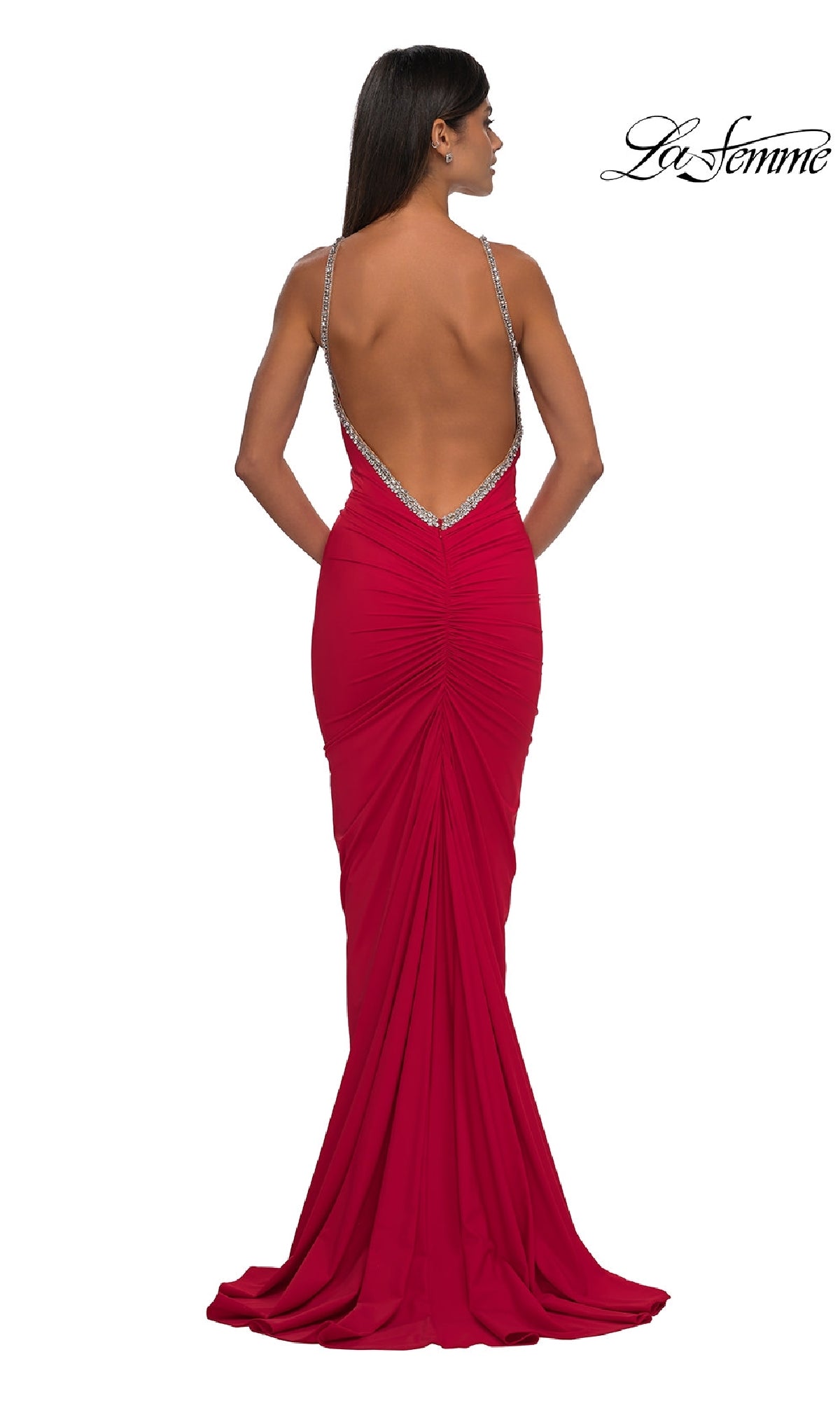 A woman models the La Femme 32970 Backless Ruched Long Prom Dress, a fitted red gown with thin embellished straps and a slight train, facing away from the camera to highlight its elegant backless design.
