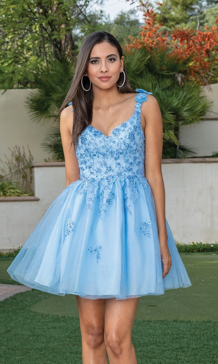 A woman stands outside in the Floral Applique Short Babydoll Glitter Hoco Dress—light blue, sleeveless, with floral embroidery and a tulle skirt. Lush greenery forms the backdrop.