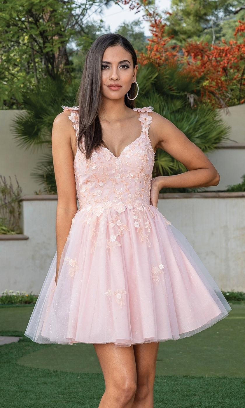 A woman stands outdoors posing with one hand on her hip, wearing the Floral Applique Short Babydoll Glitter Hoco Dress featuring light pink floral embroidery and a tulle skirt.