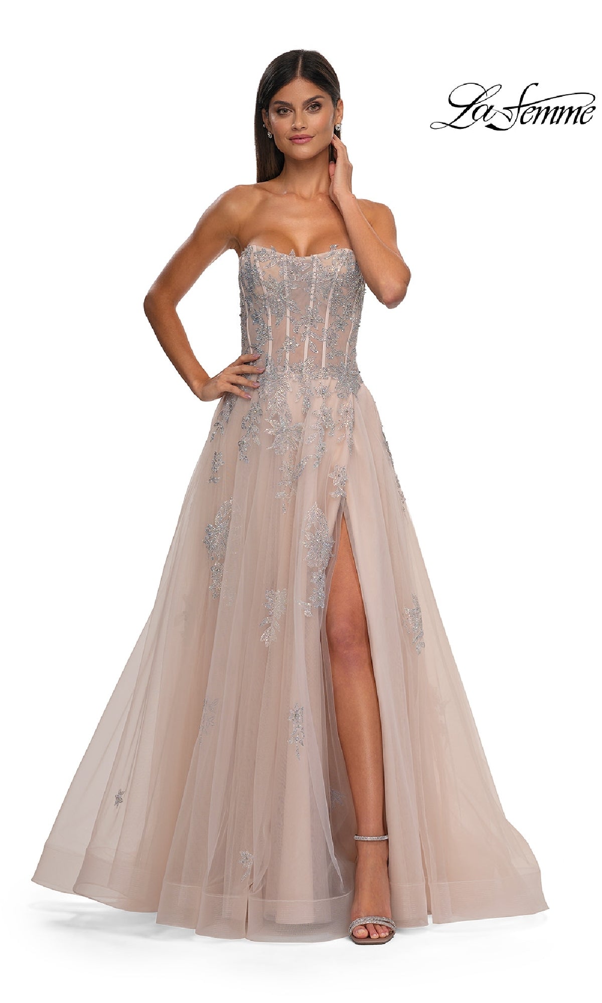 A woman wears the La Femme 33028 strapless beaded long prom gown, featuring rhinestone floral appliques, a corset-style sheer bodice, high slit, and metallic heels.