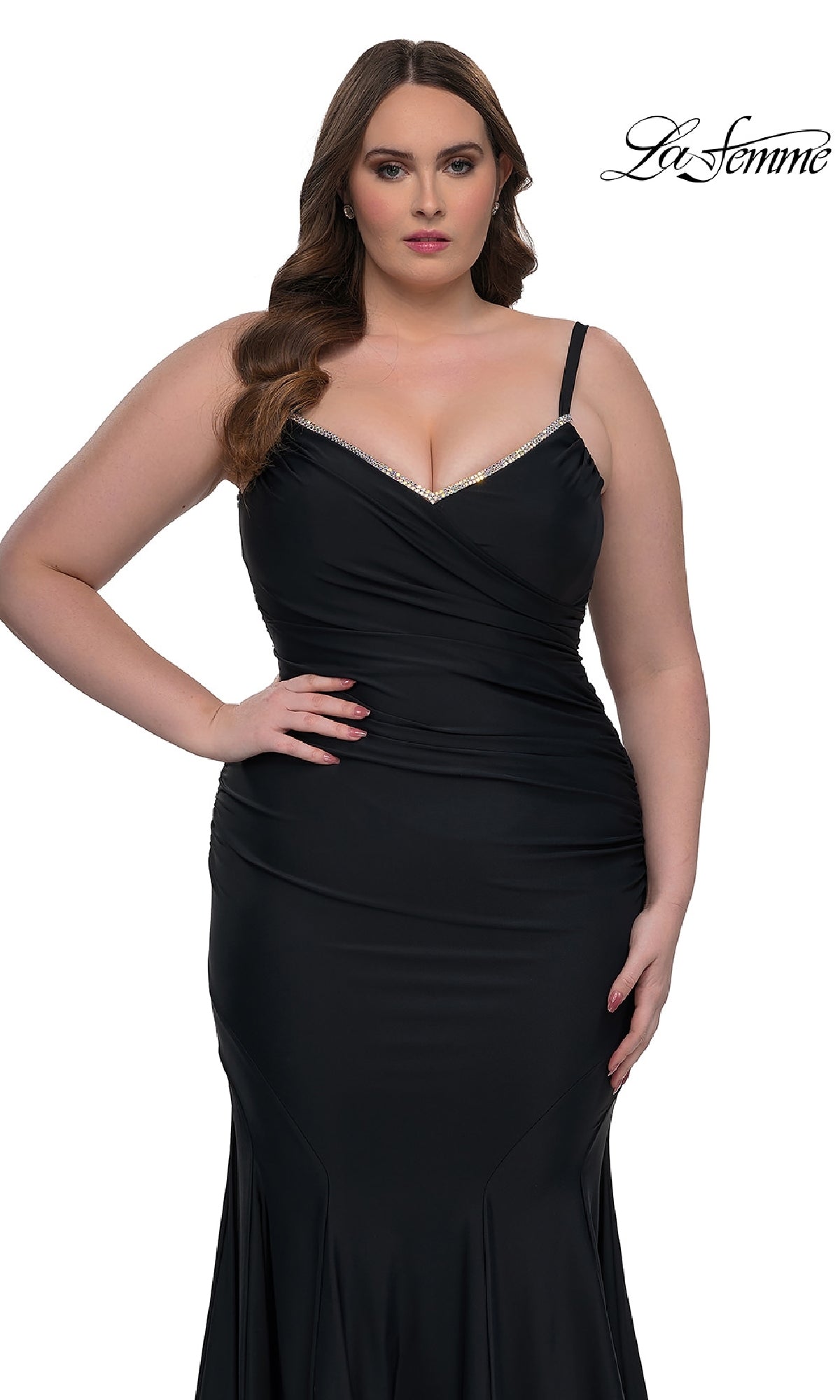 A woman poses against a white background in the La Femme 33057 plus-size floor-length prom dress, a fitted black gown with thin straps, a slight v-neckline, and subtle rhinestone accents. The
