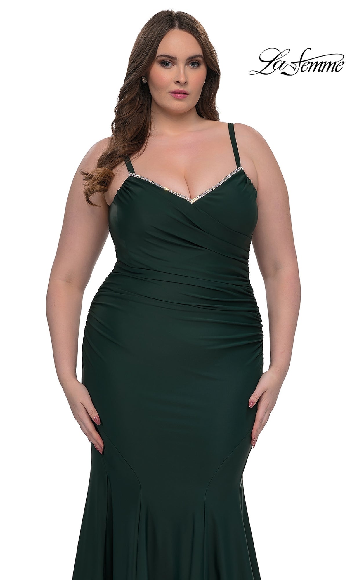 A woman wears the fitted dark green La Femme 33057 plus-size floor-length prom dress with thin straps and ruched details. She stands against a white background with