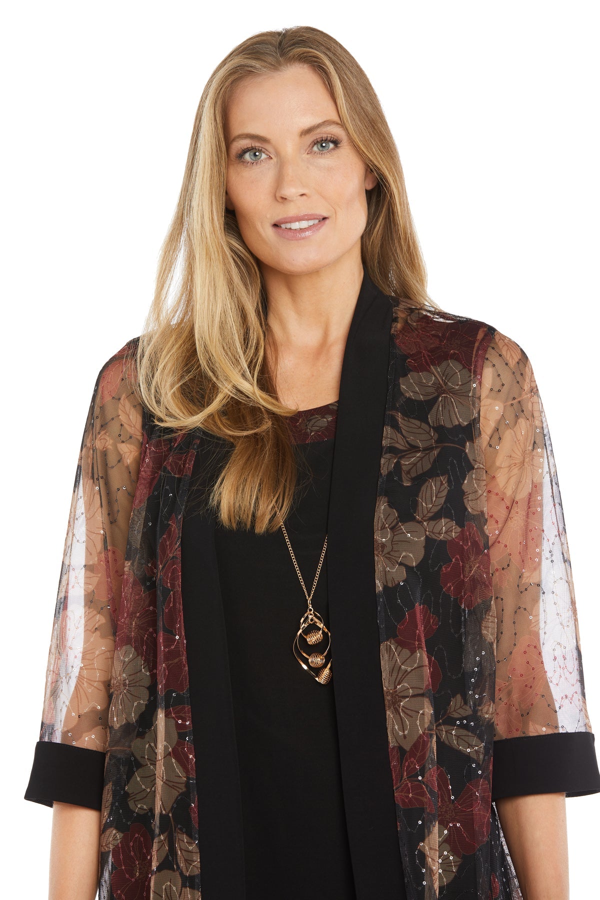 A woman with long blonde hair models the R&M Richards 3312 Petite Two-Piece Party Dress, featuring a black semi-formal style and sheer floral-patterned shawl, accessorized with a long pendant necklace against a white background.