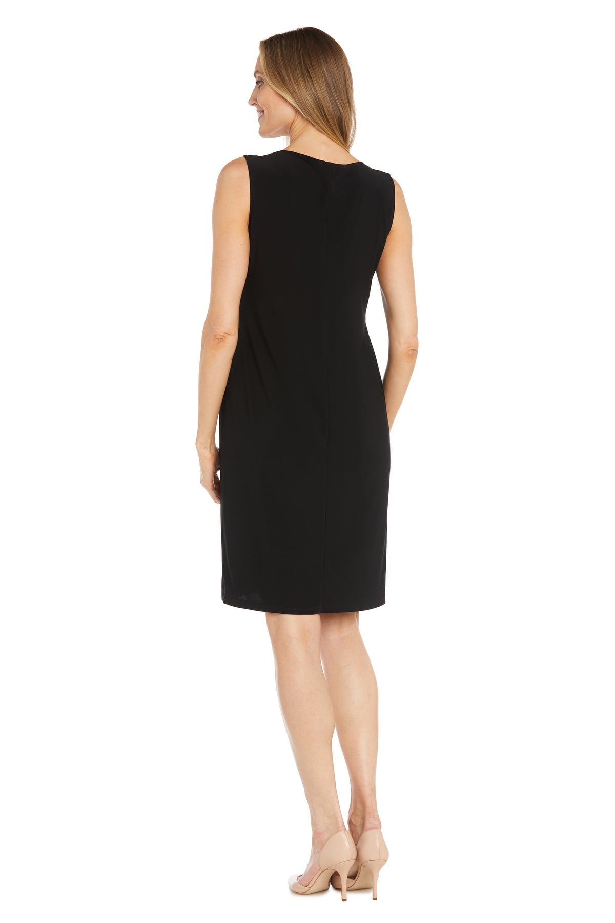 A woman faces away in the R&M Richards 3312 Petite Two-Piece Party Dress, a sleeveless black knee-length semi-formal outfit paired with beige heels against a white background.