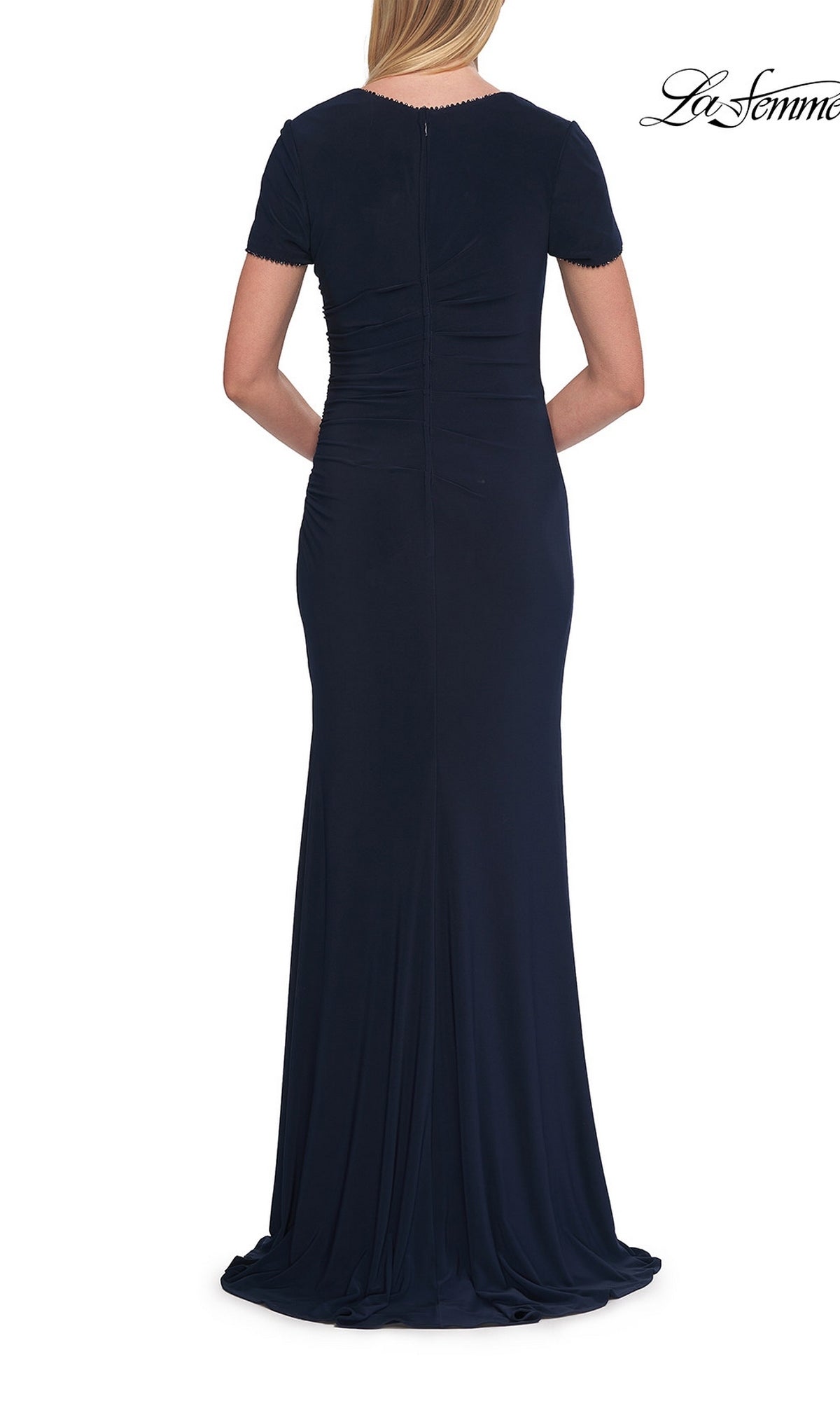 A woman is seen from the back wearing the La Femme 33146 Short Sleeve Long Jersey Formal Dress in navy blue. This formal dress showcases subtle ruching at the waist and a fitted, floor-length silhouette.