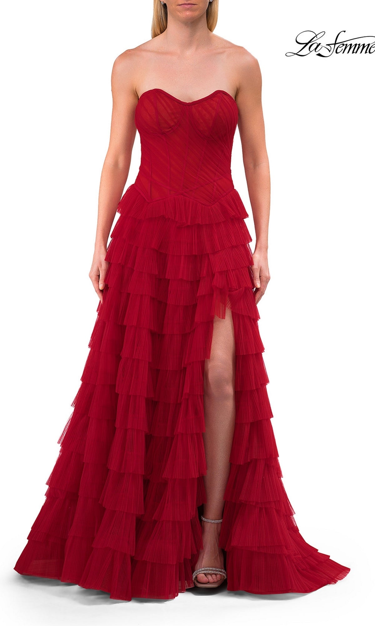 A woman wearing the La Femme 33202, a red strapless ruffle prom ball gown with a sweetheart neckline, floor-length layered ruffles, and a thigh-high slit, stands against a white background.