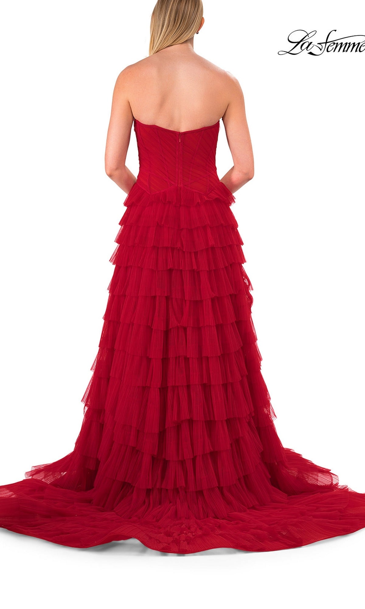 A woman in a La Femme 33202 Strapless Ruffle Prom Ball Gown with layered tulle ruffles stands facing away from the camera against a white background.