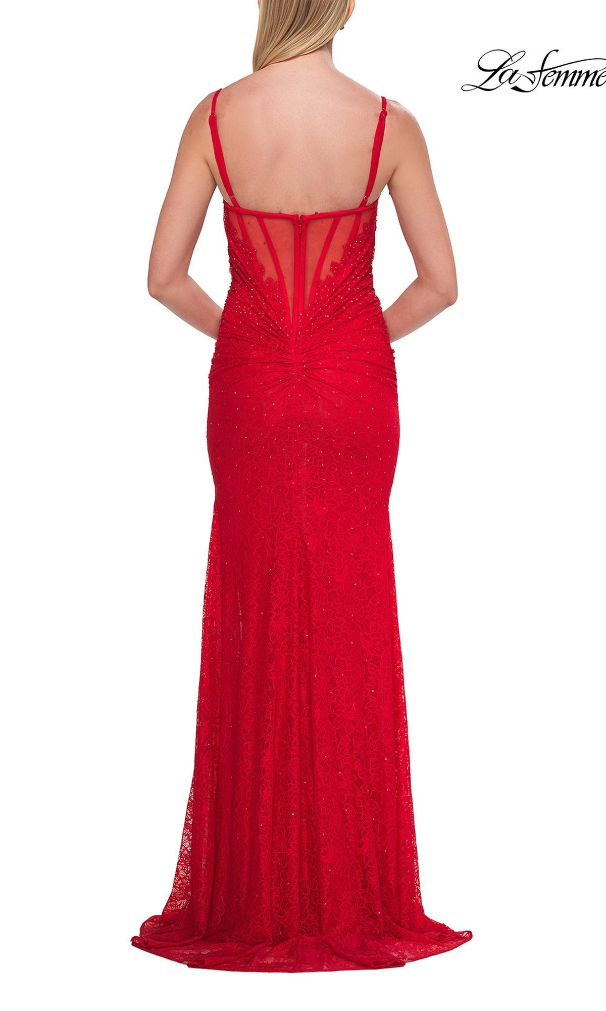A woman wearing the La Femme 33305 long prom dress—a fitted, floor-length red lace gown with thin straps, a corset bodice, and an open back—stands facing away from the camera.