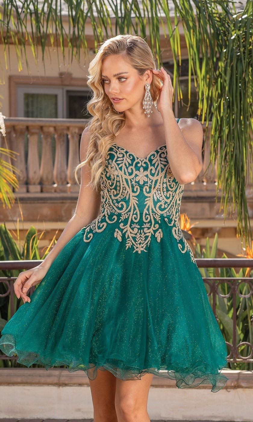 A woman stands outdoors near palm trees, touching her earring and looking to the side, wearing the Gold-Embroidered Short Homecoming Dress 3330—a green and gold strapless dress with gold embroidery and a flared skirt.