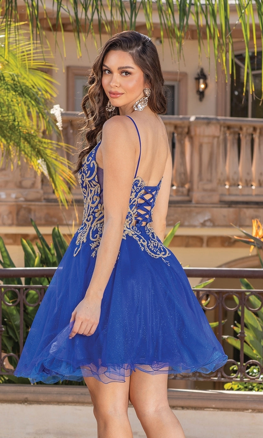 A woman stands outdoors, looking over her shoulder, wearing the Gold-Embroidered Short Homecoming Dress 3330—a blue, sleeveless dress with gold embroidery and a lace-up back.