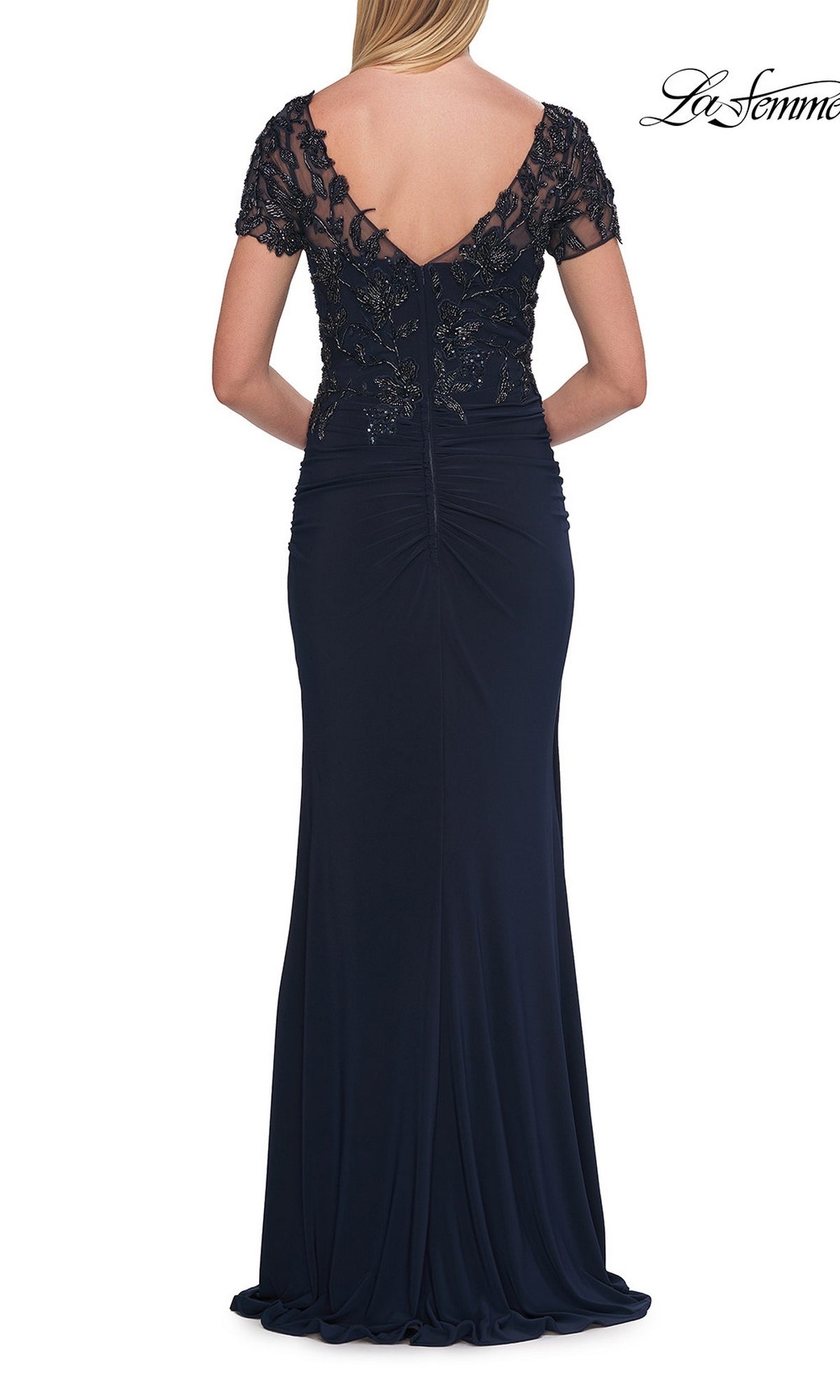 Woman in the La Femme 33332 Short-Sleeve Beaded Lace Formal Gown, a floor-length navy blue mother of the bride dress with short lace sleeves and beaded detailing, shown from the back.