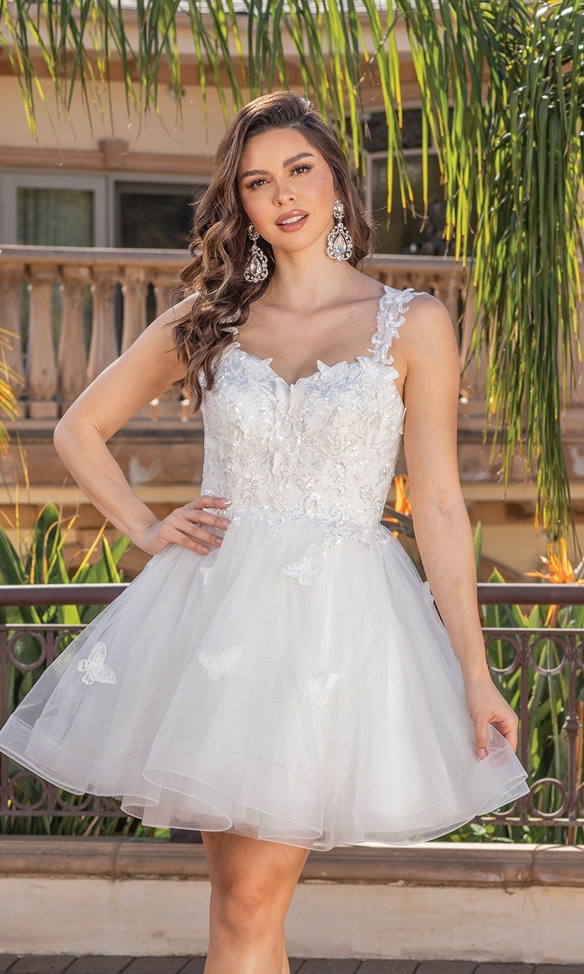 A woman stands outdoors near a railing, wearing the Embroidered-Lace Short Babydoll Hoco Dress 3338—a short white semi-formal party dress adorned with floral lace and butterfly embellishments.