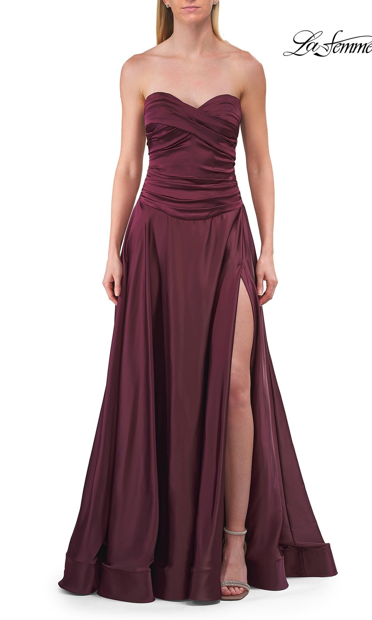 A woman wearing the La Femme 33417 Strapless Sweetheart Prom Gown in dark berry, featuring a ruched bodice and high slit, stands against a white background.