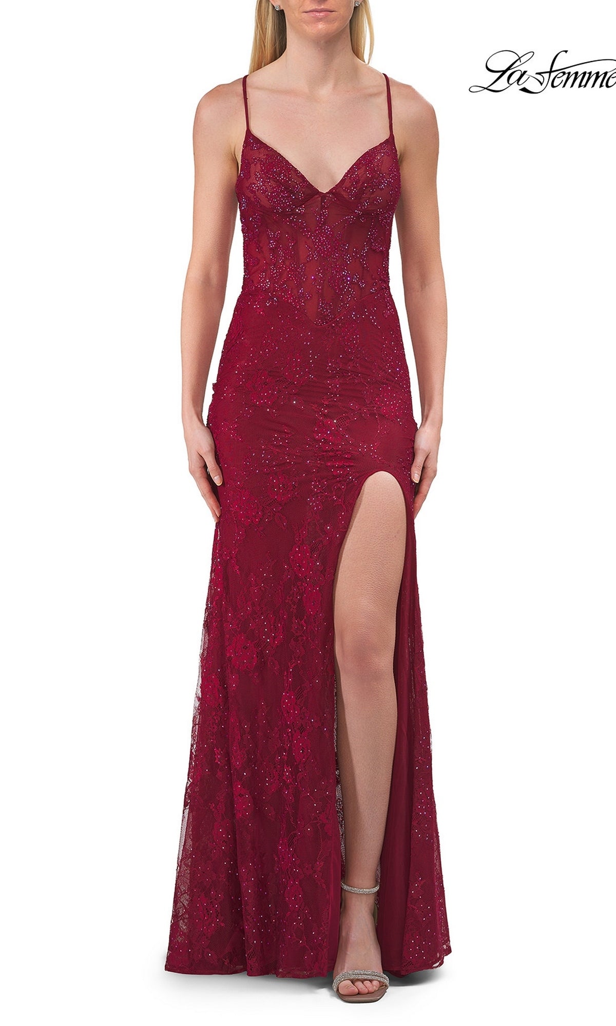 A woman wearing the La Femme 33473 Long Beaded Floral Lace Prom Dress in raspberry, featuring a sleeveless design with thin straps, beaded floral lace, a sheer corset bodice, and a high slit, stands against a white background.