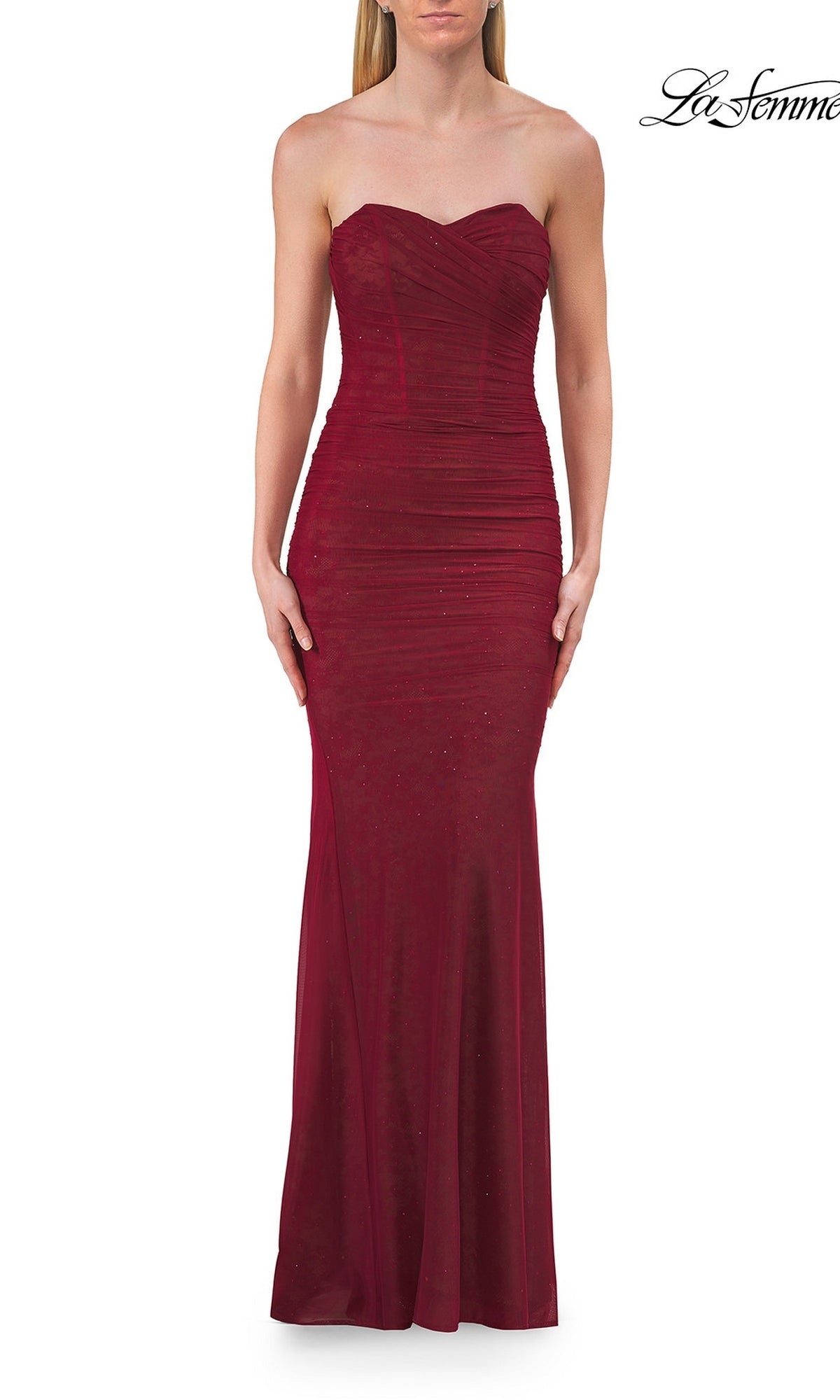 A woman wearing the Classic Strapless Long Prom Dress La Femme 33601—a floor-length, fitted raspberry gown with ruched detailing and subtle embellishments—stands against a white background.