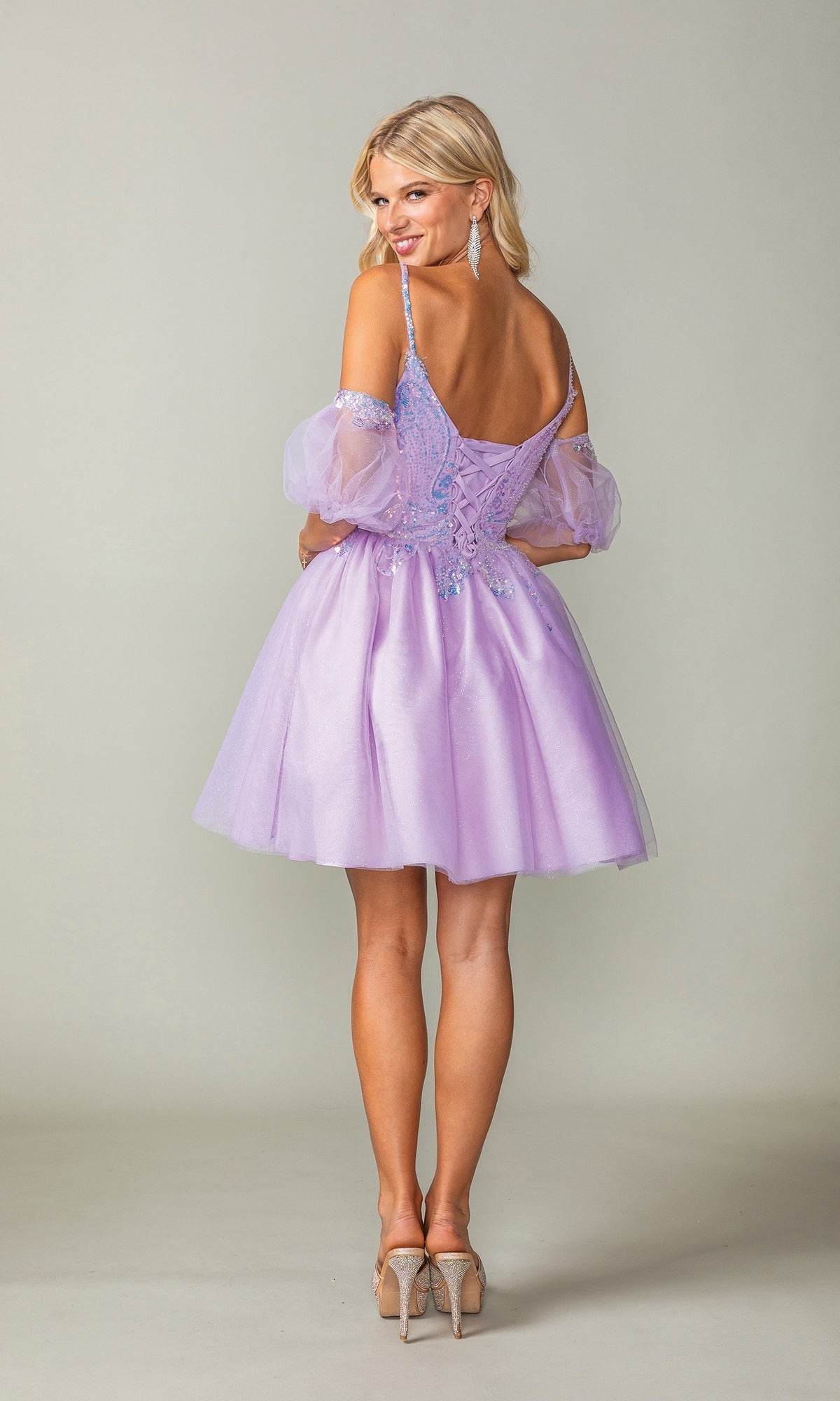 A woman in the Puff-Sleeve Short Purple Homecoming Dress 3362 stands with her back to the camera, turns her head, and smiles, showing off the dress’s elegant silhouette against a plain background.