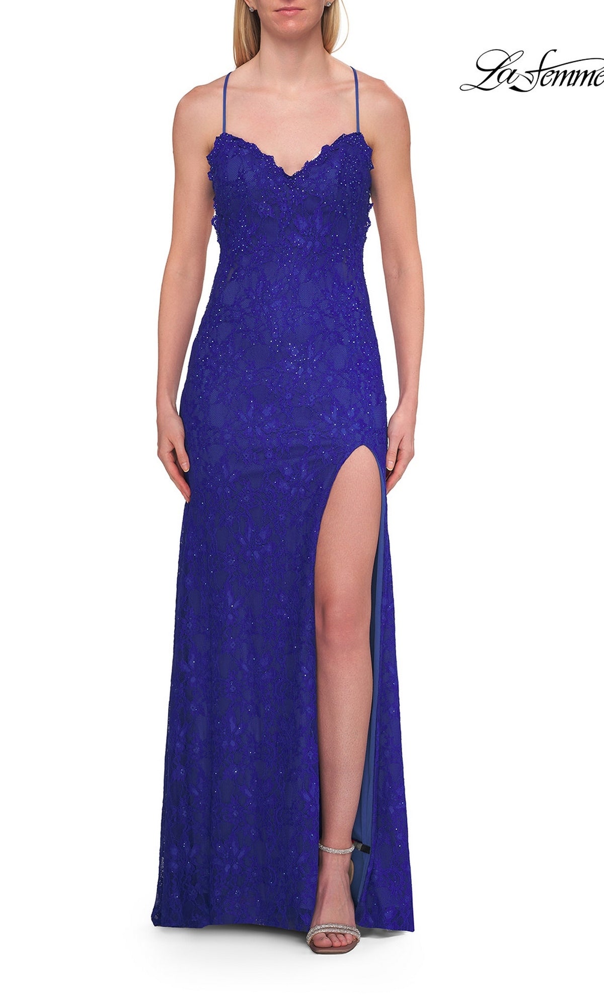 A woman stands against a white background wearing the Beaded Long Lace Prom Dress: La Femme 33647 in royal blue, which features delicate lace with beaded accents, thin straps, a sweetheart neckline, and a high slit. She completes the look with open-toe heels.