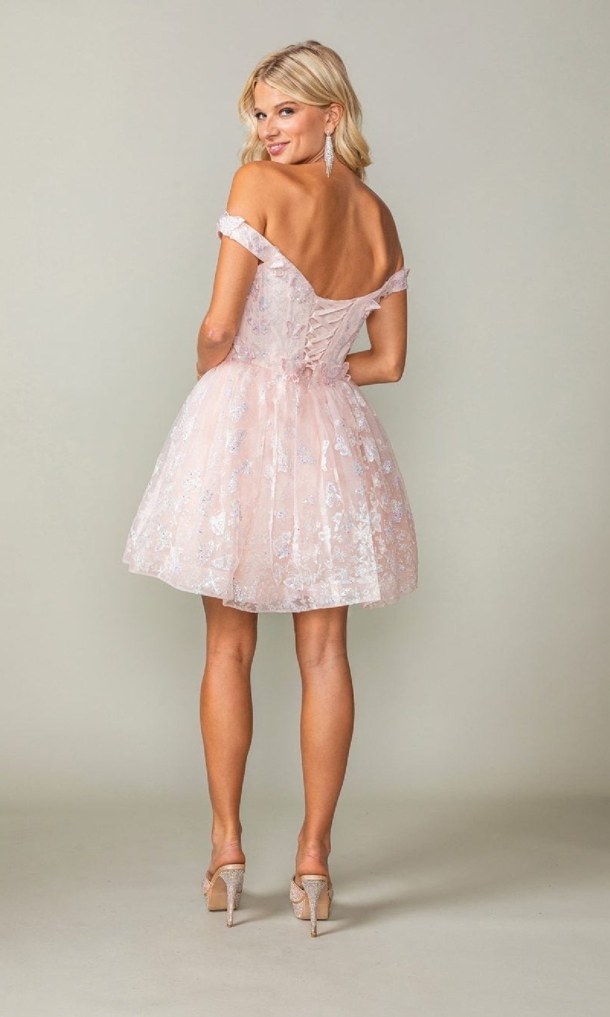 Woman wearing a light pink lace dress with a backless design on a plain background
