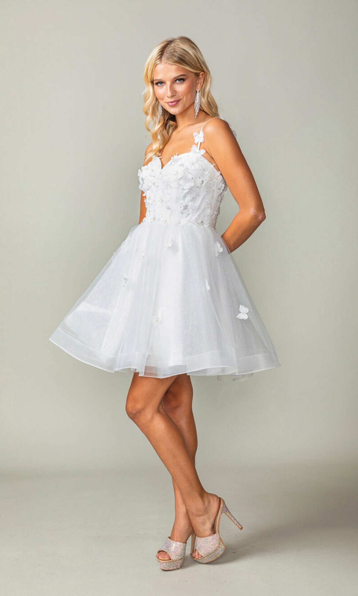 A woman in the Lace-Up Short Butterfly Homecoming Dress 3369, a white semi-formal dress with delicate 3-D butterflies, and high heels stands against a plain light background.