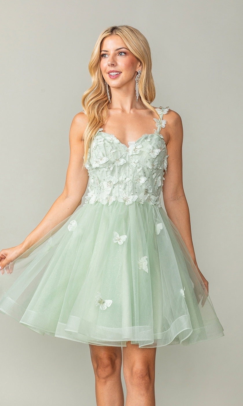 A woman wears the Lace-Up Short Butterfly Homecoming Dress 3369, a light green knee-length semi-formal dress featuring floral appliqués and 3-D butterflies on a tulle skirt, standing against a plain background.