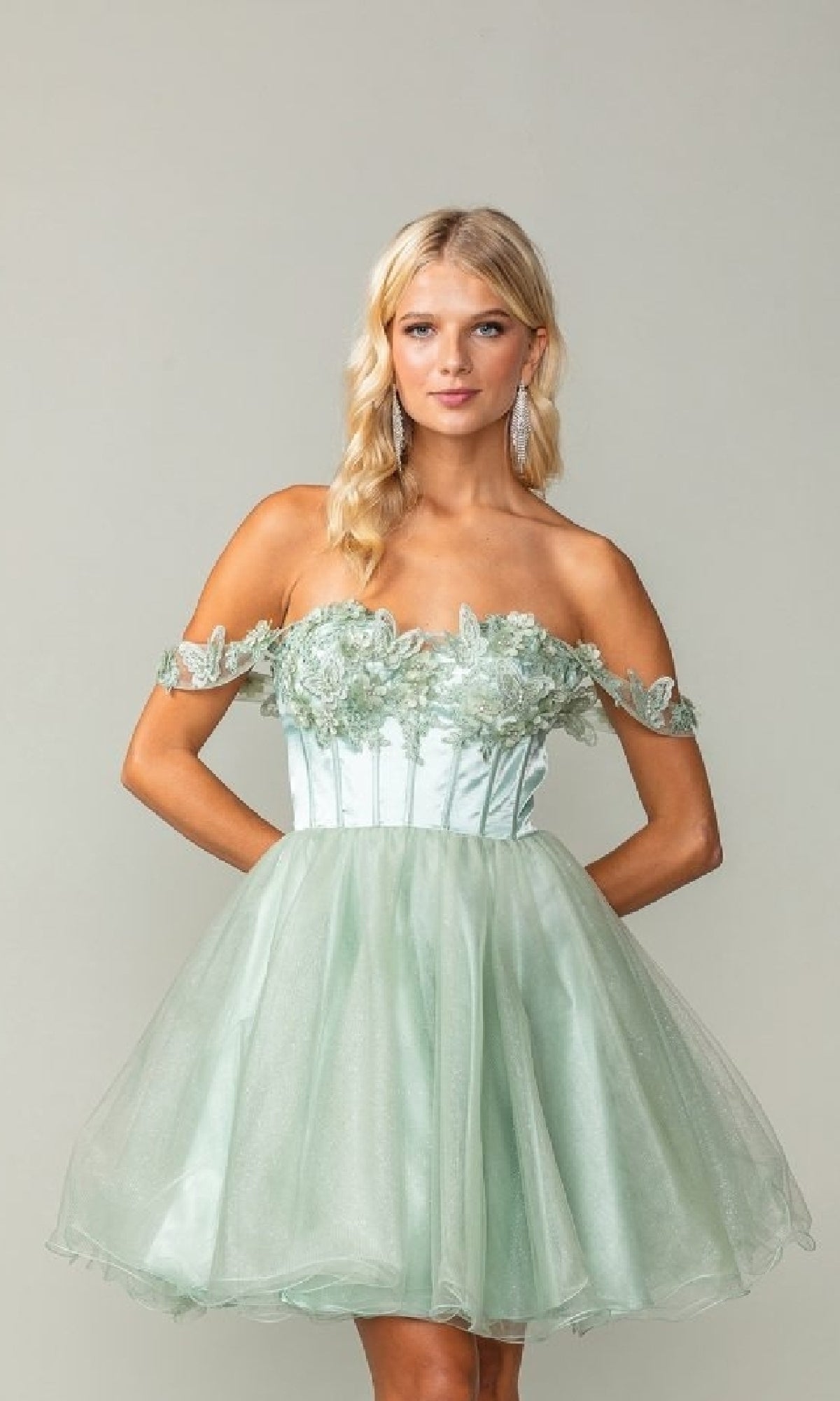 Woman wearing a light green off-shoulder dress with floral embellishments against a plain background