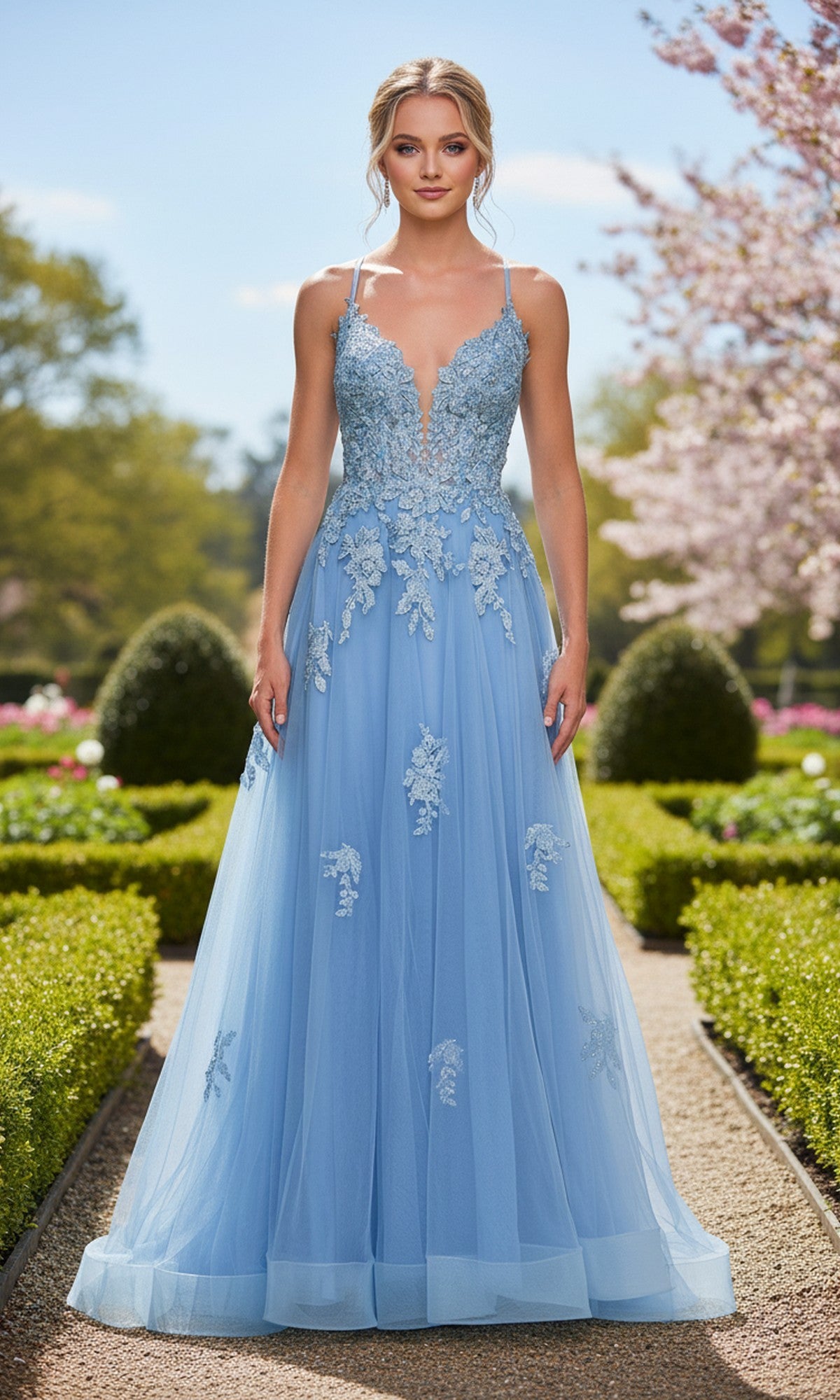A woman stands outdoors in a garden, wearing the light blue La Femme 33716 Lace-Embroidered Prom Ball Gown with floral appliques and thin straps.