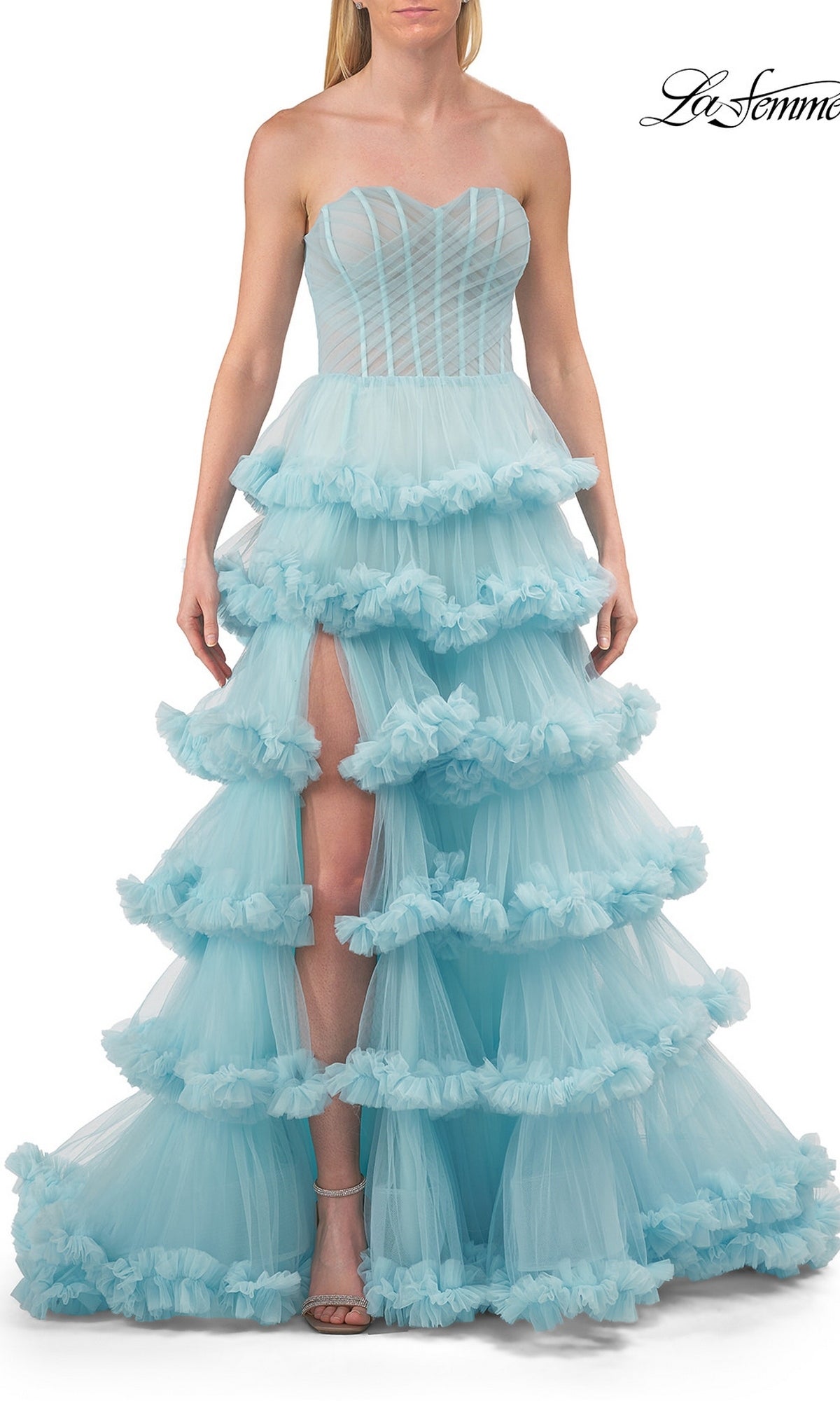 A woman wearing the Strapless Tiered Prom Ball Gown: La Femme 33717 in Cloud Blue—a ball gown with a corset-style bodice, sweetheart neckline, tiered skirt, and front slit—standing against a white background.