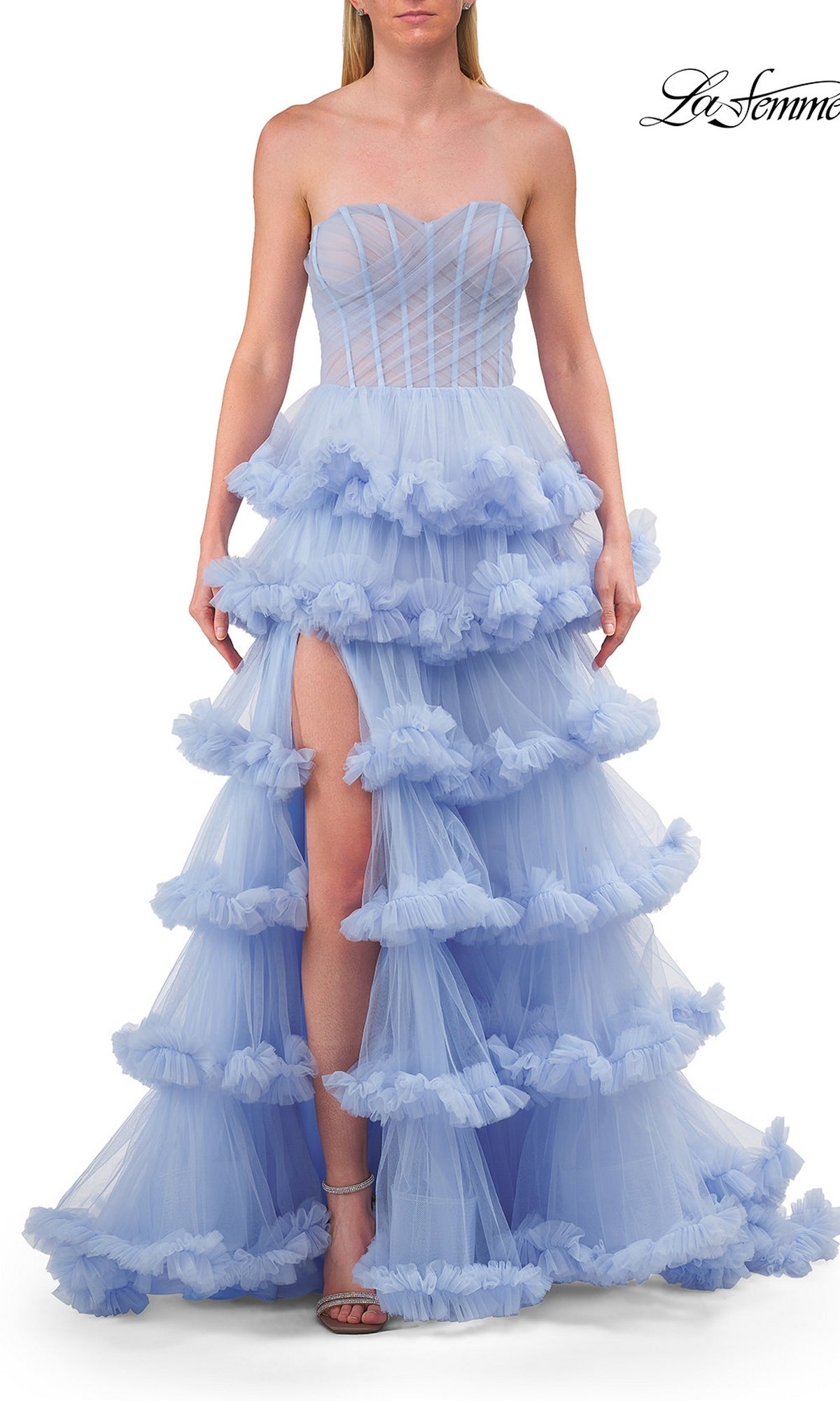 A woman wearing the Strapless Tiered Prom Ball Gown: La Femme 33717 in light periwinkle, featuring a strapless sweetheart neckline, tiered tulle layers, and a thigh-high slit, stands against a white background.
