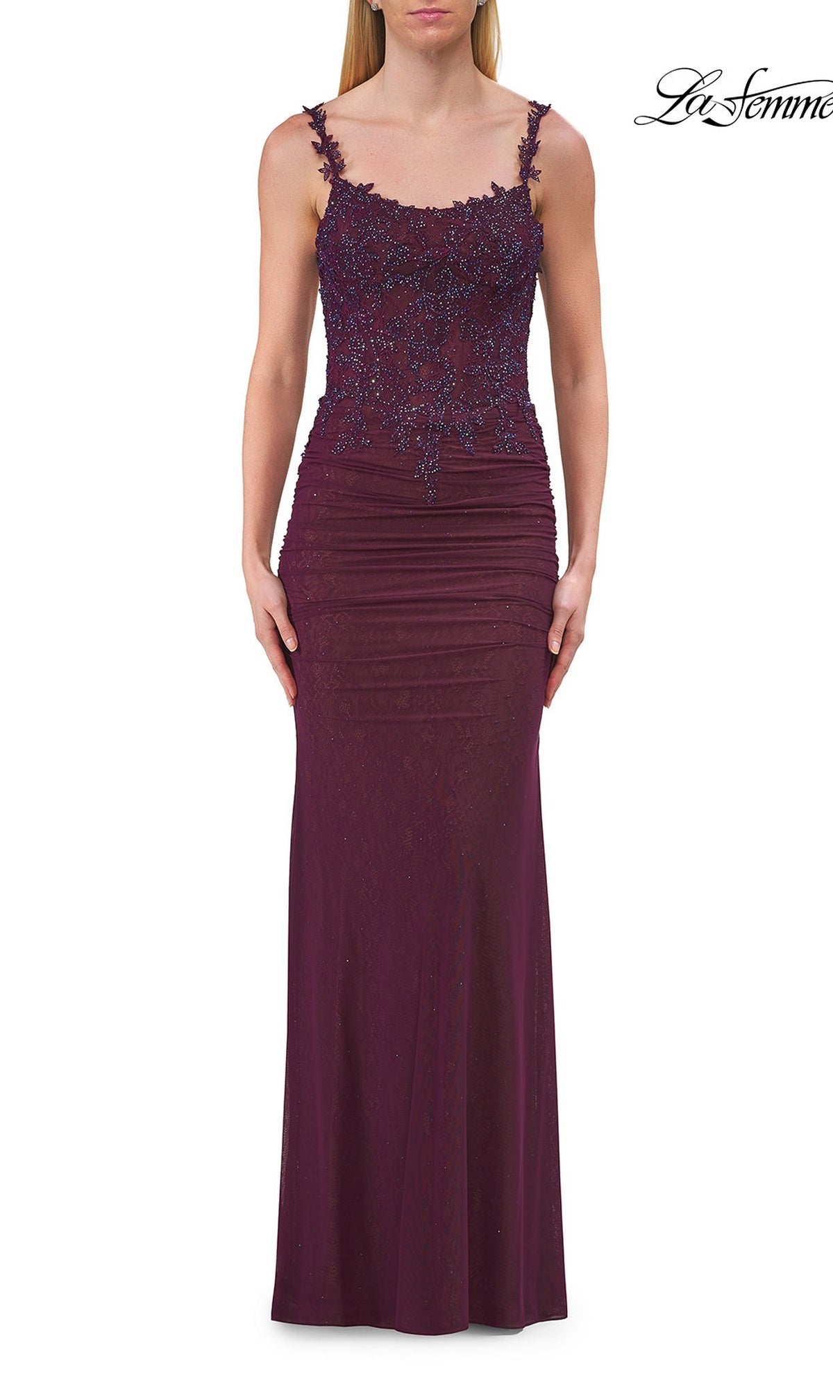A woman wearing a sleeveless, floor-length dark berry La Femme 33721 open-back sheer-corset prom gown, featuring lace and beaded detailing, stands against a white background.