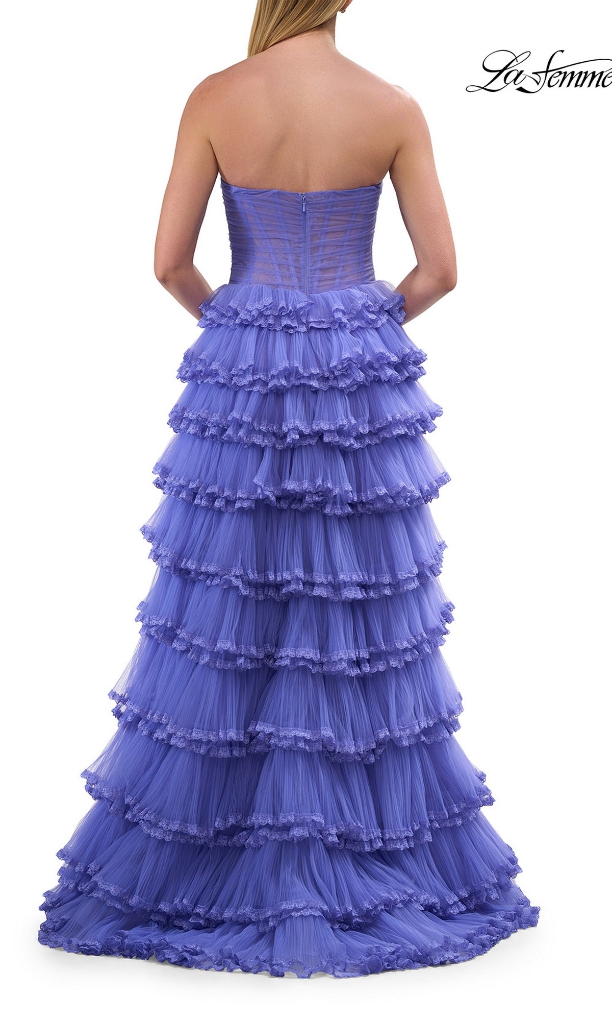 Wearing the La Femme 33727 long prom dress, a woman stands with her back to the camera, showcasing the strapless, tiered tulle ball gown with a corset bodice and layers of ruffled purple fabric cascading elegantly to the floor.