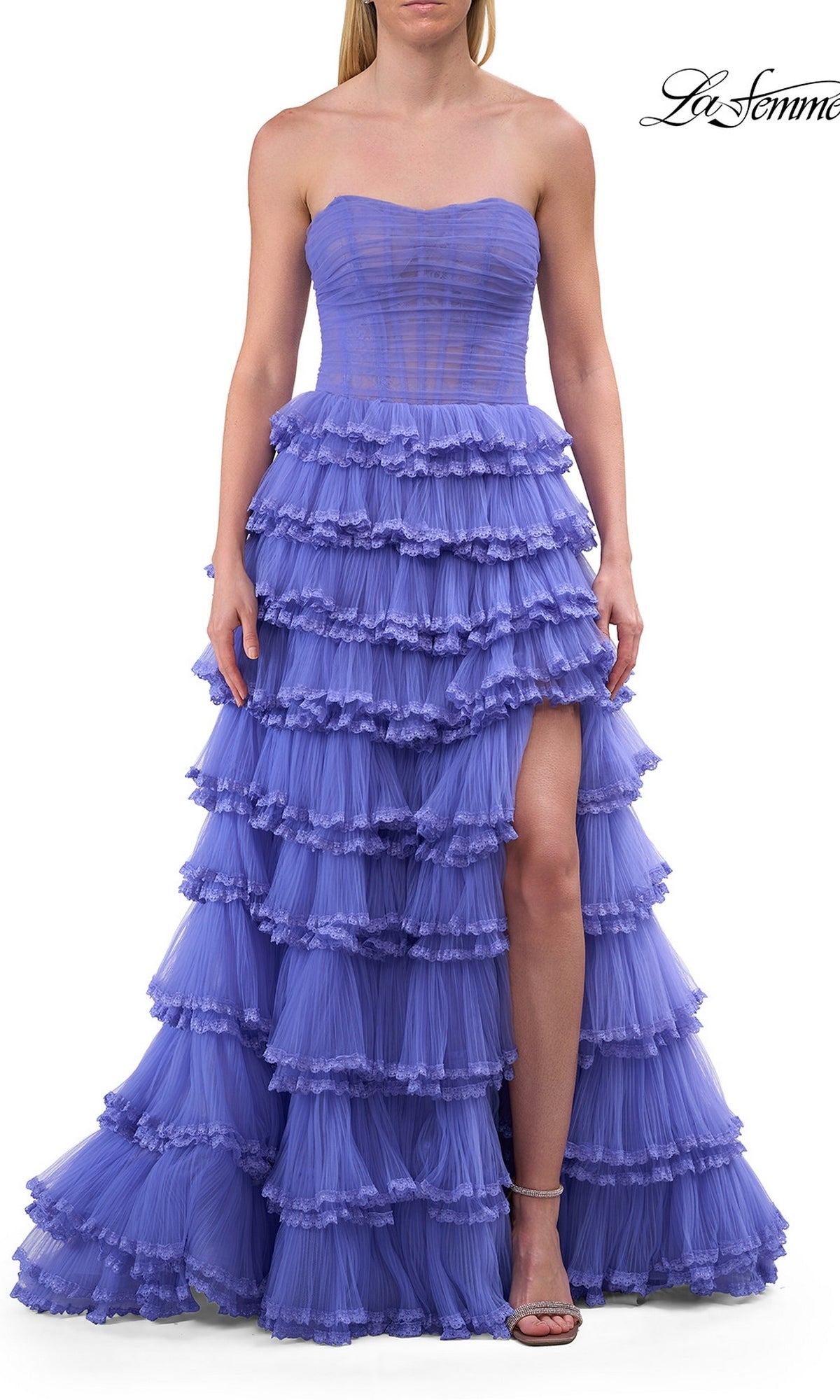 A woman wears the La Femme 33727 long prom dress in periwinkle, featuring a strapless ruffled design, a sheer corset bodice, and a thigh-high slit, while standing against a white background.