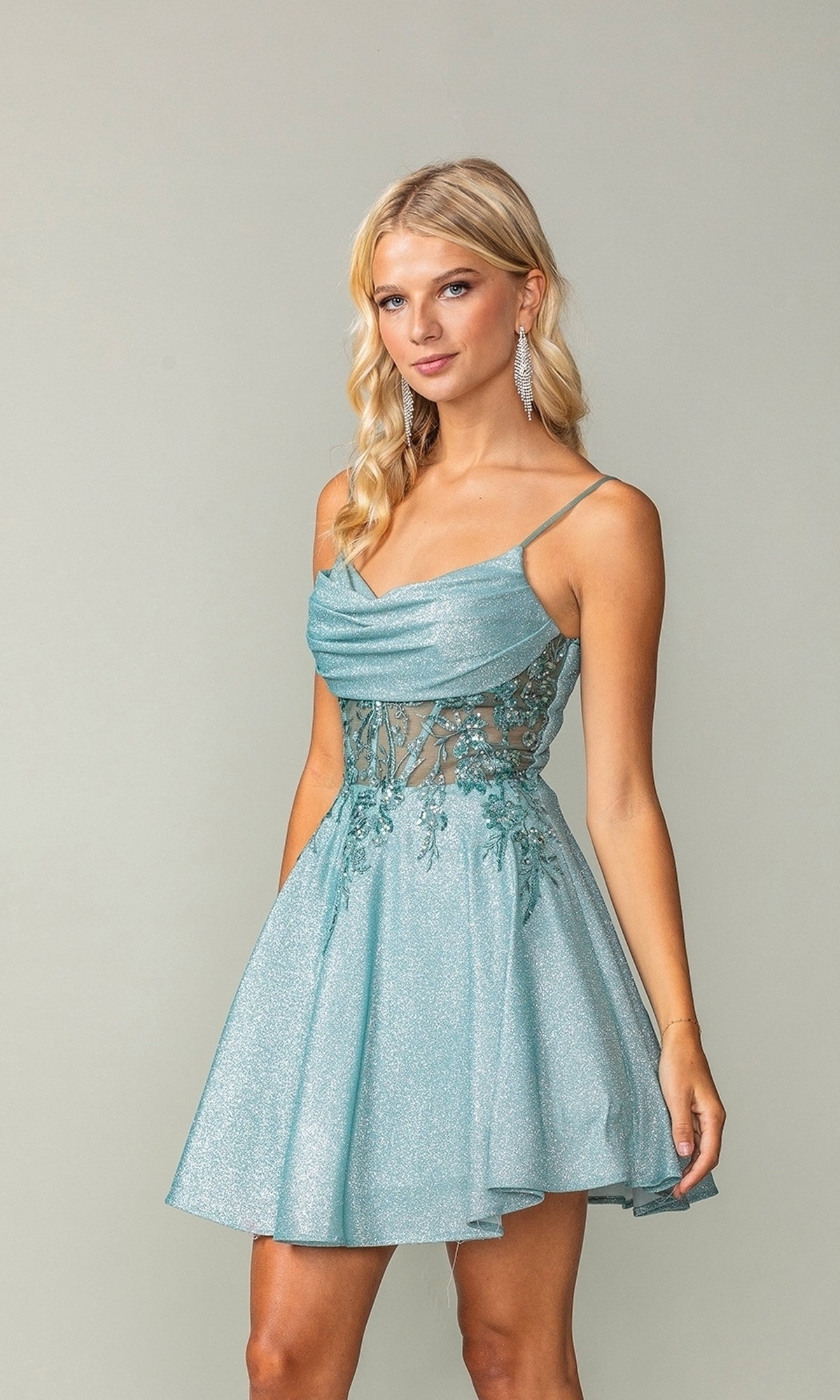 A woman models the Cowl-Neck Short Glitter Homecoming Dress 3386, a light blue, sleeveless mini dress with spaghetti straps, lace bodice, cowl neckline, and flared skirt against a plain background.