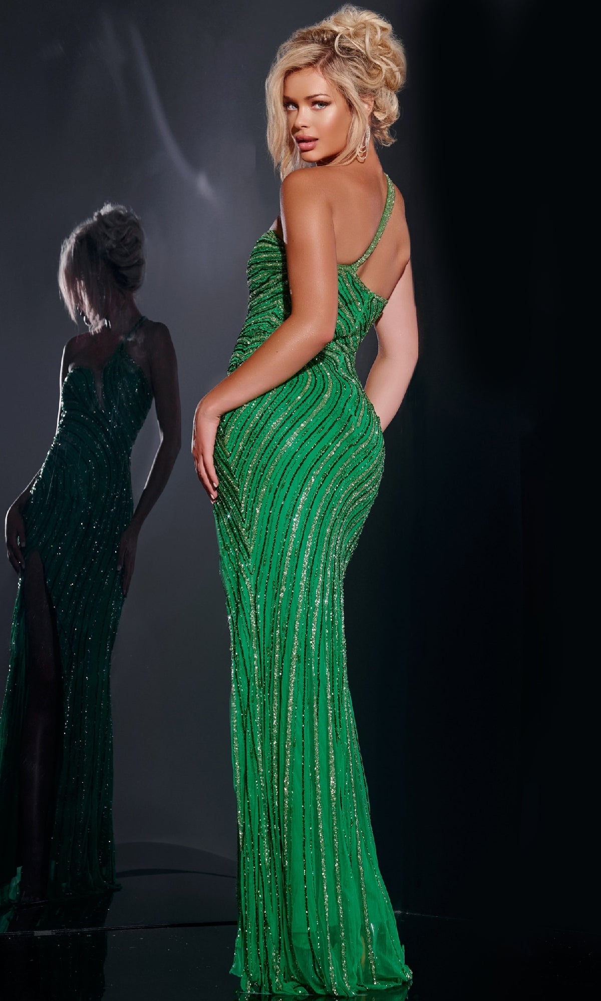 A woman poses with hand on hip in the Jovani 34010 long prom dress—an elegant, one-shoulder sequin gown with a thigh-high slit—while her reflection is visible in the mirror behind her.