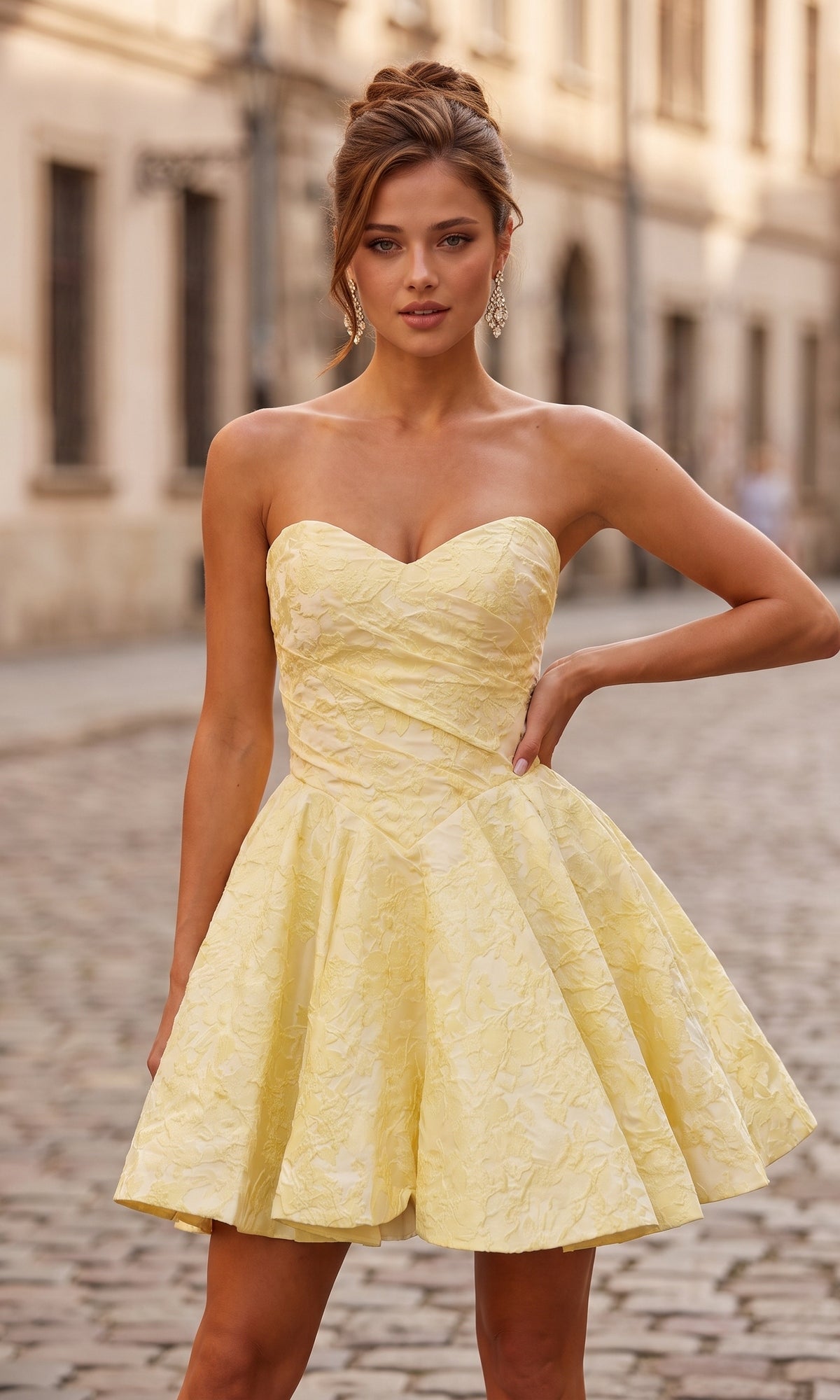 A woman wearing the yellow Strapless Mini Floral Hoco Dress (La Femme 34147) stands on a cobblestone street with buildings in the background.