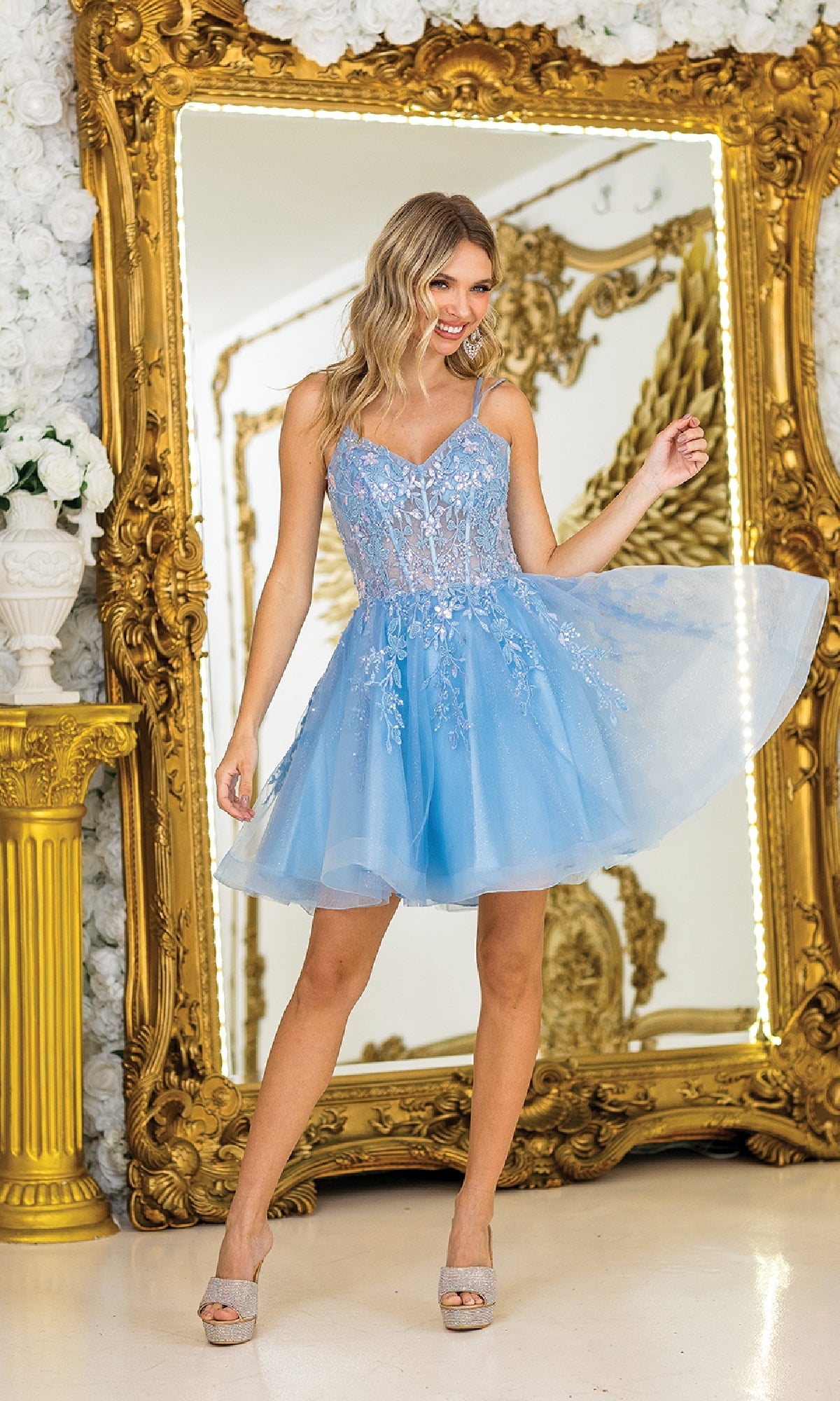 A woman in the Short Corset Prom Dress: Dancing Queen 3415—a light blue, sleeveless, embroidered floral A-line dress—poses before a large ornate gold mirror.