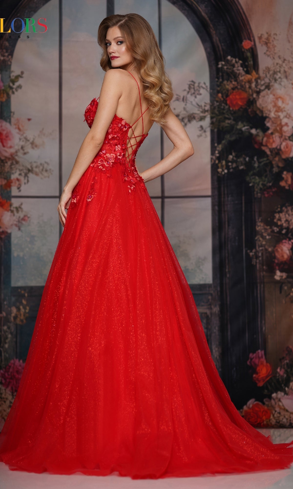 A woman in a Pastel Long Prom Ball Gown (Colors Dress 3496) stands before a floral and window backdrop, facing slightly away from the camera.