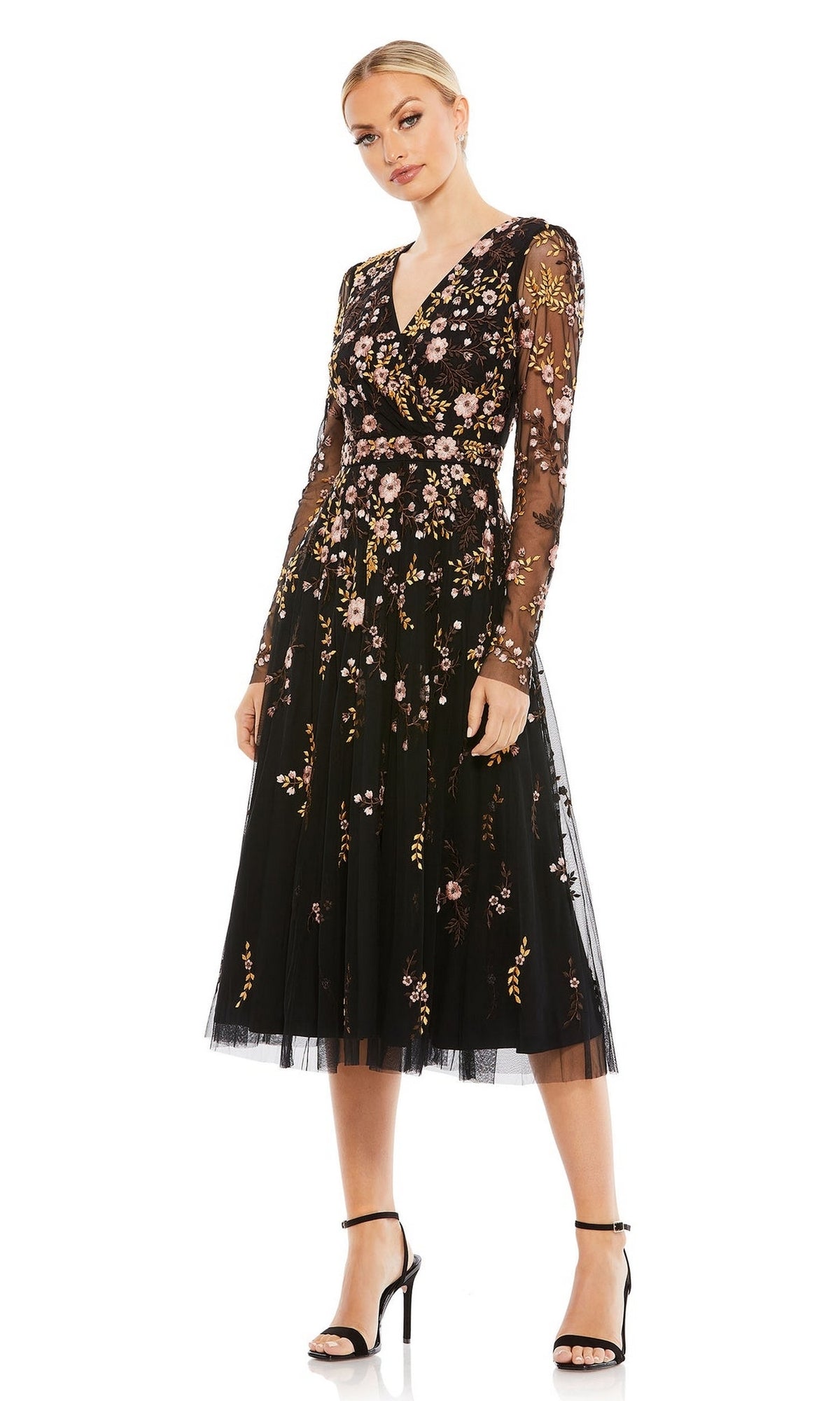 A woman models the Midi Floral Wedding Guest Dress by Mac Duggal—black, long sleeve, with floral embroidery—paired with black strappy heels against a plain white background.