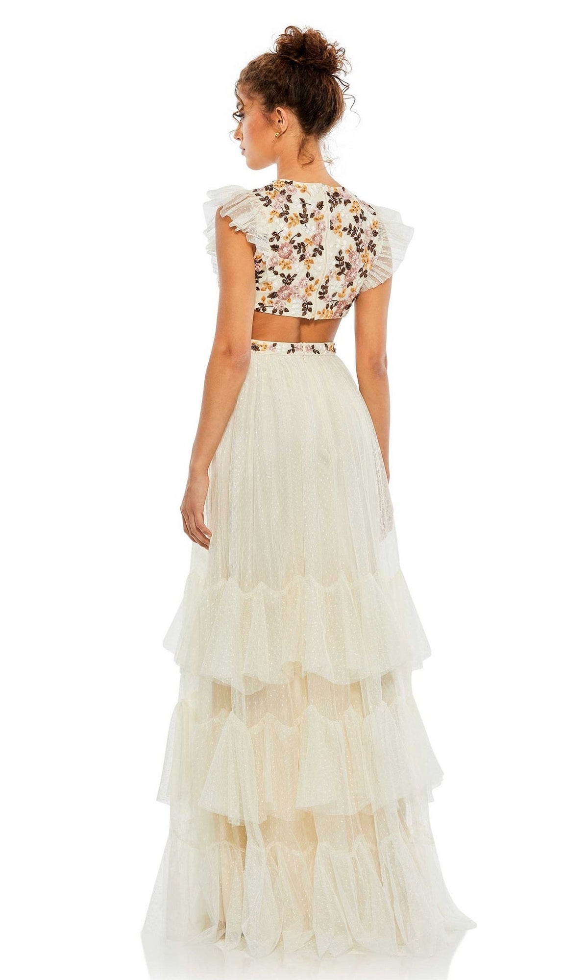 A woman stands with her back to the camera, wearing the Long Formal Dress 35106 by Mac Duggal—a tiered gown with a white crop top, floral embroidery, and elegant ruffle sleeves.