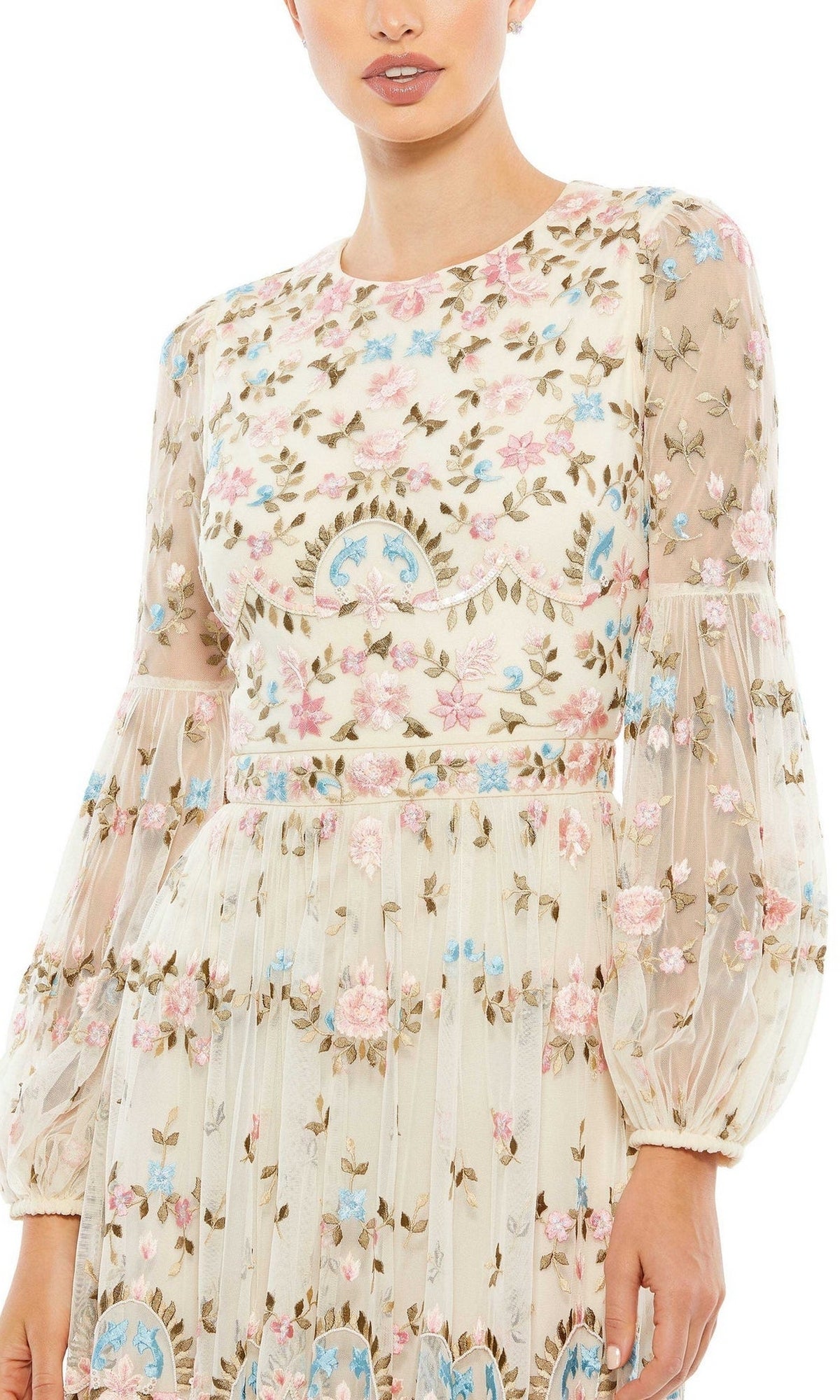A woman wears the Long Formal Dress 35111 by Mac Duggal, featuring cream-colored fabric with pink, blue, and green floral embroidery. The fitted bodice, sheer long sleeves, and floor-length design create an elegant formal look.