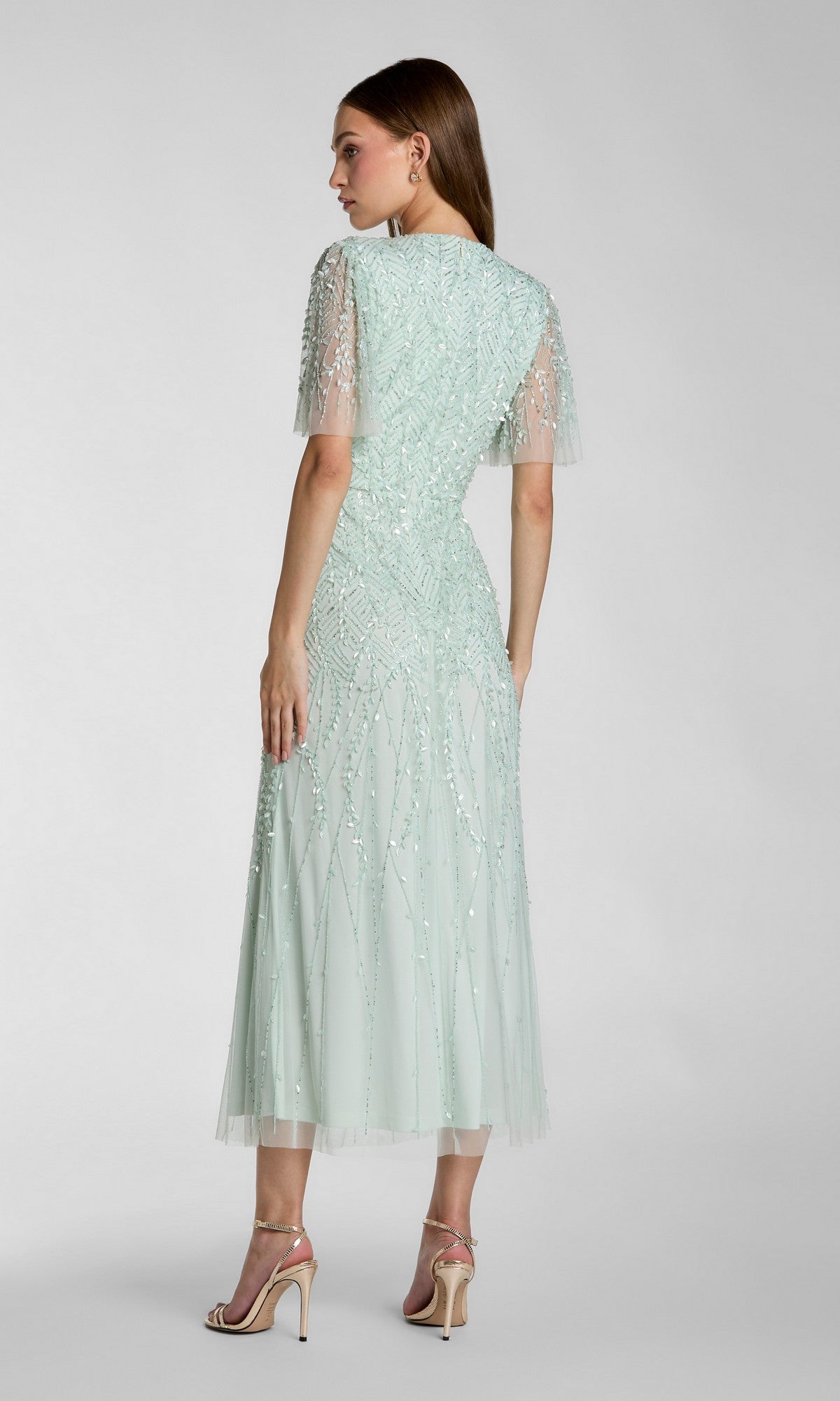 A woman wears the Mac Duggal 35116 Beaded Midi Semi-Formal Dress in light mint green with short sleeves and nude heels, posing against a plain background—a stylish option for any semi-formal occasion.