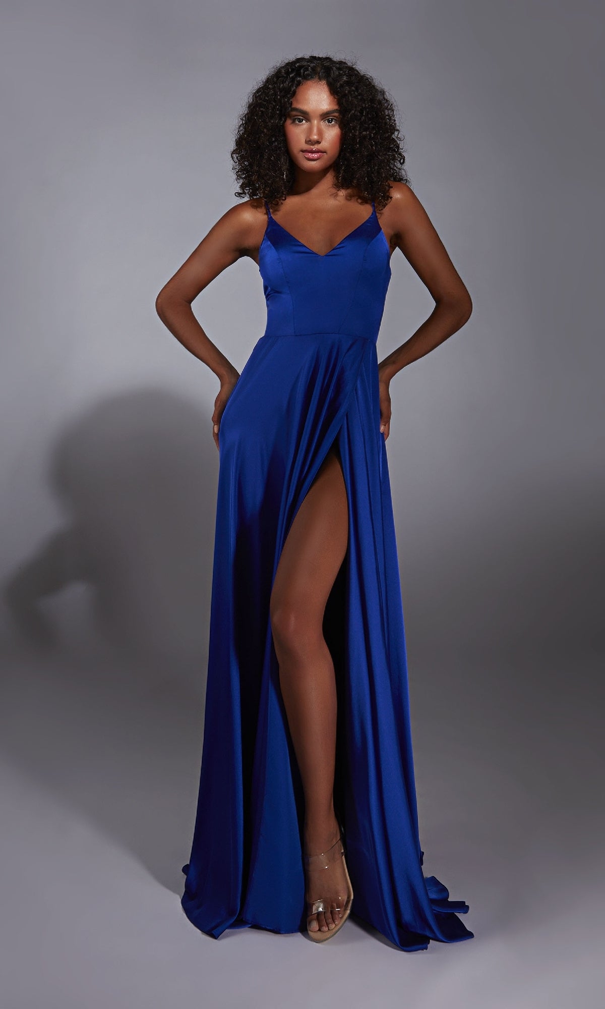 A woman models the Aerie Couture 354, a sleeveless, floor-length royal blue satin prom dress with an elegant leg slit, standing against a plain gray background.