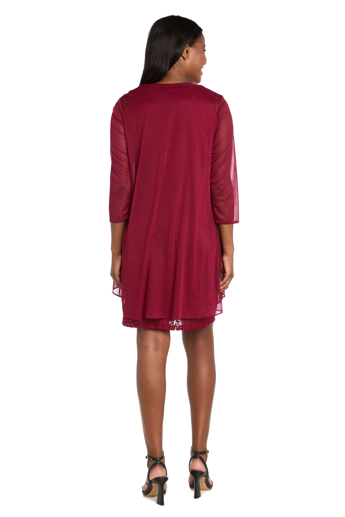 A woman stands facing away, wearing the R&M Richards 3594 short semi-formal jacket dress in burgundy with sheer three-quarter sleeves and black heeled sandals.