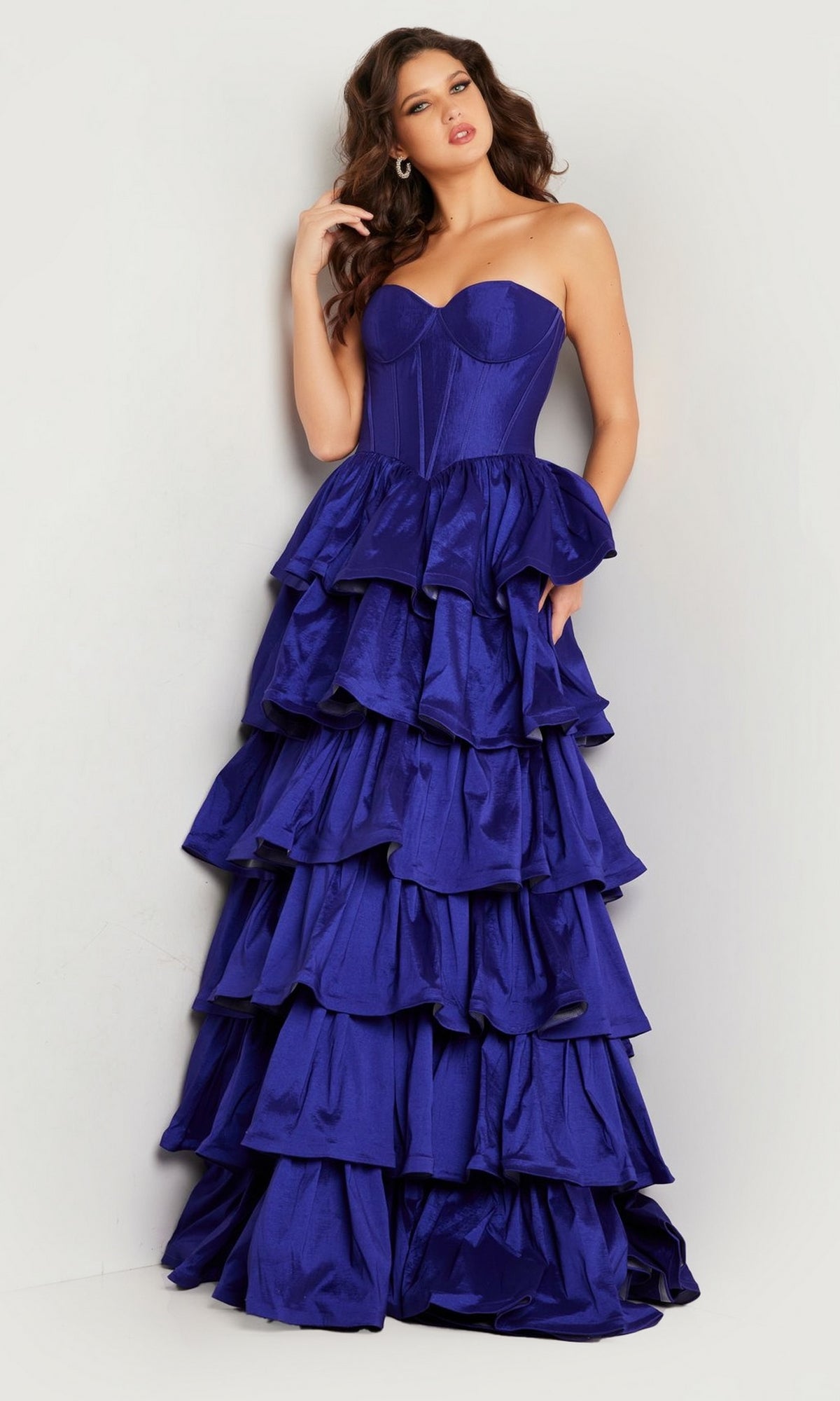 A woman in the Jovani 36619 Strapless Ruffled Prom Ball Gown—royal blue with a fitted bodice and layered ruffle skirt—stands against a light background.